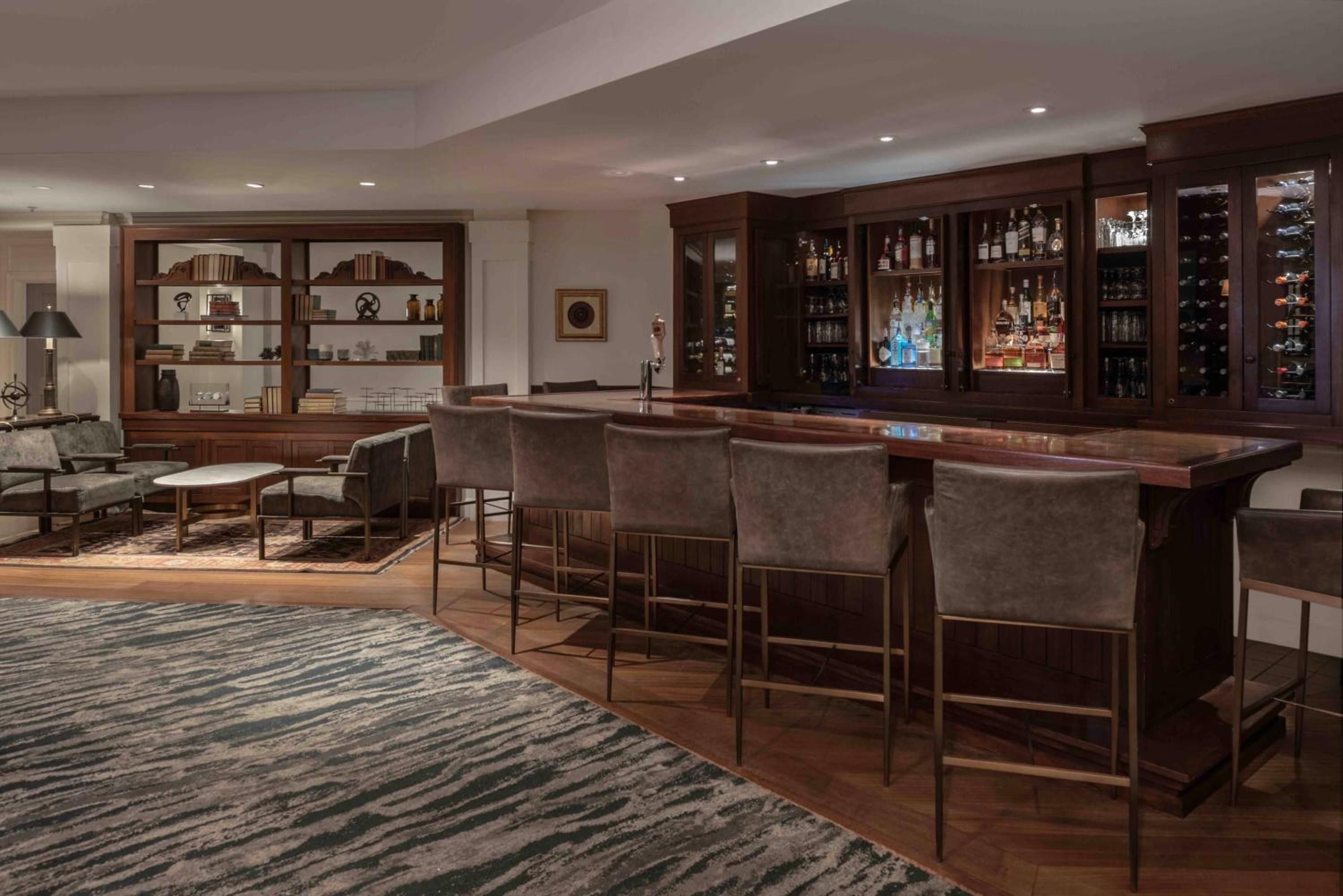 Rich walnut cabinetry frames an impressive spirits collection while plush leather barstools invite lingering conversations over craft cocktails in this sophisticated basement retreat.