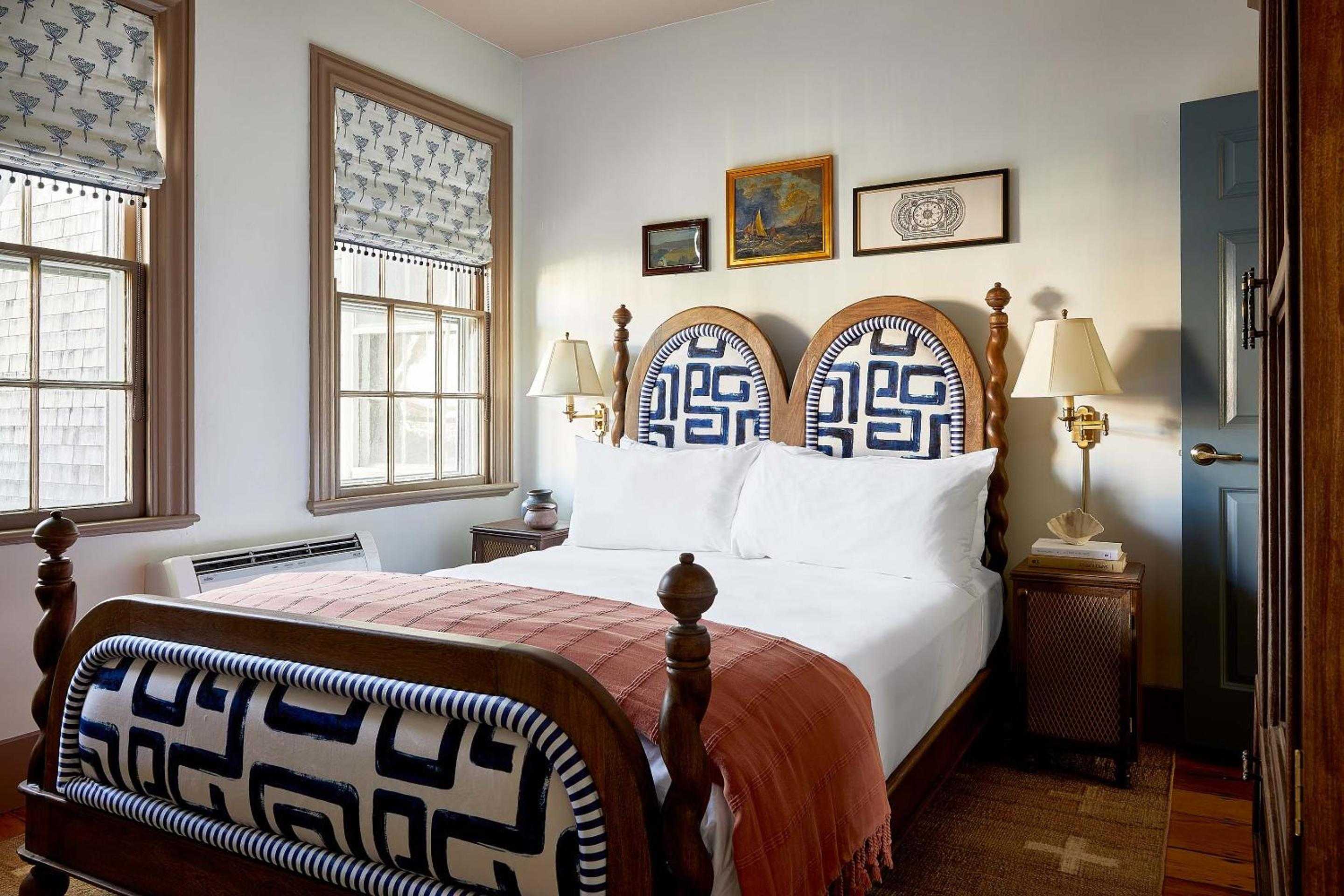 Nautical-inspired textiles meet rustic charm in this intimate guest room, where blue Greek key patterns frame crisp white linens and golden afternoon light streams through weathered shingle views.