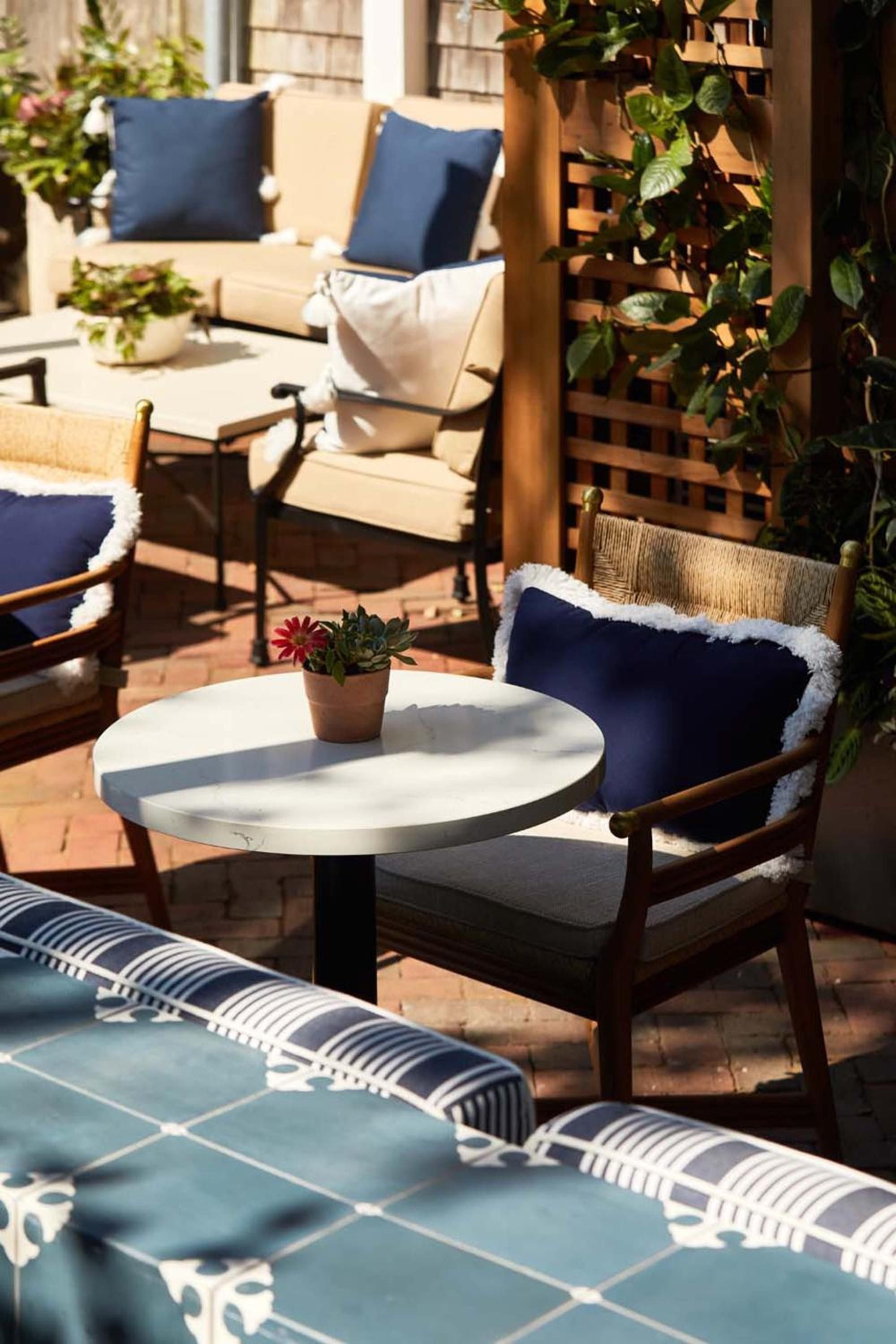 Afternoon light dances across the tiled pool deck where navy cushioned chairs and climbing vines create intimate pockets of Mediterranean-inspired tranquility.
