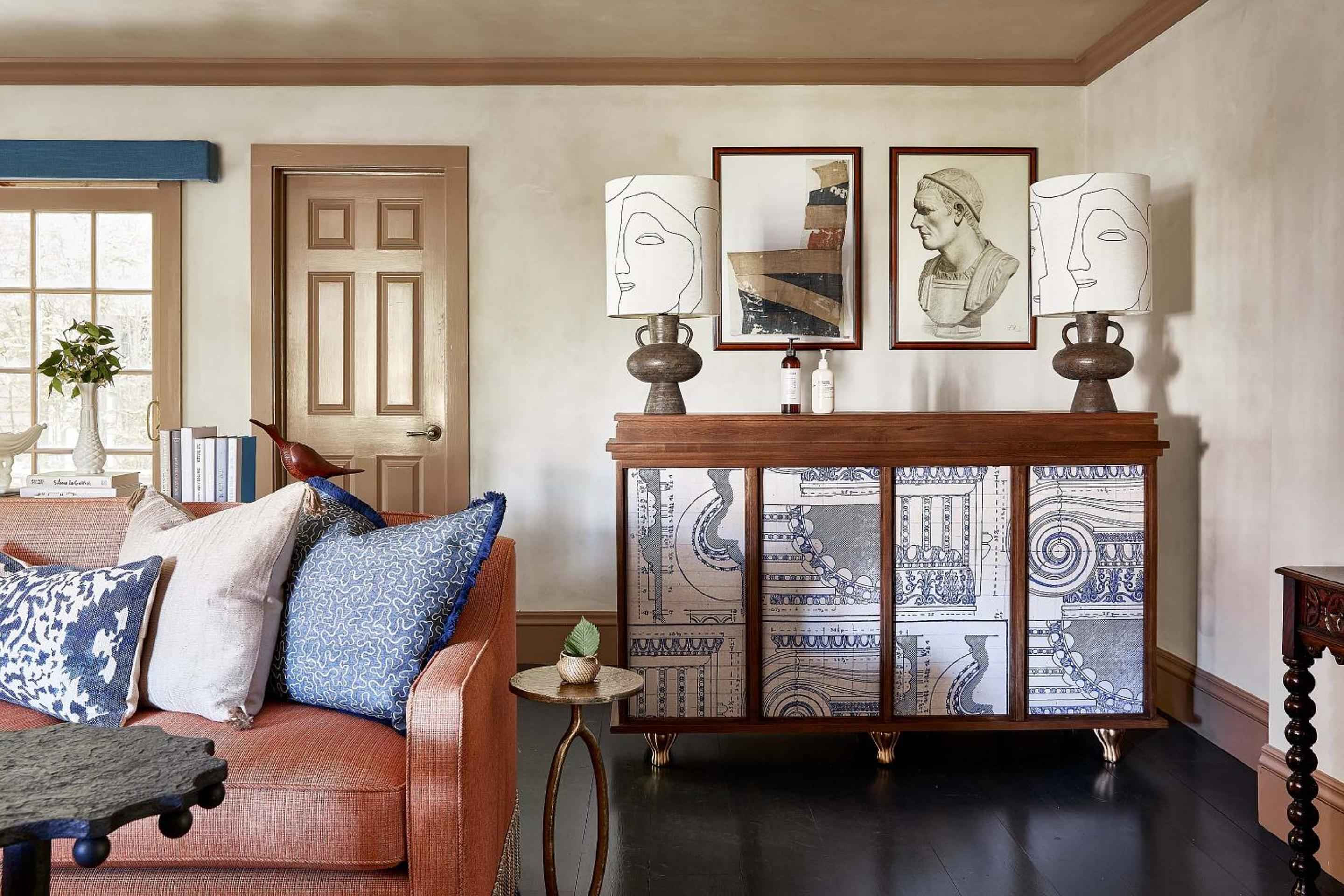 Curated art prints and patterned textiles create an intimate living space where burnt orange seating meets sculptural ceramics against warm neutral walls.