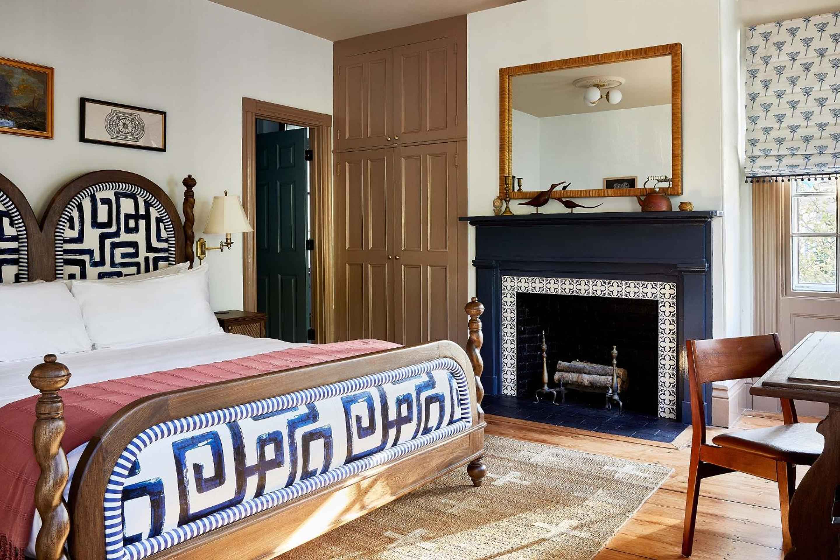 Greek key patterns dance across woven headboards while a crackling fireplace casts golden light on weathered wood floors and hand-thrown pottery.