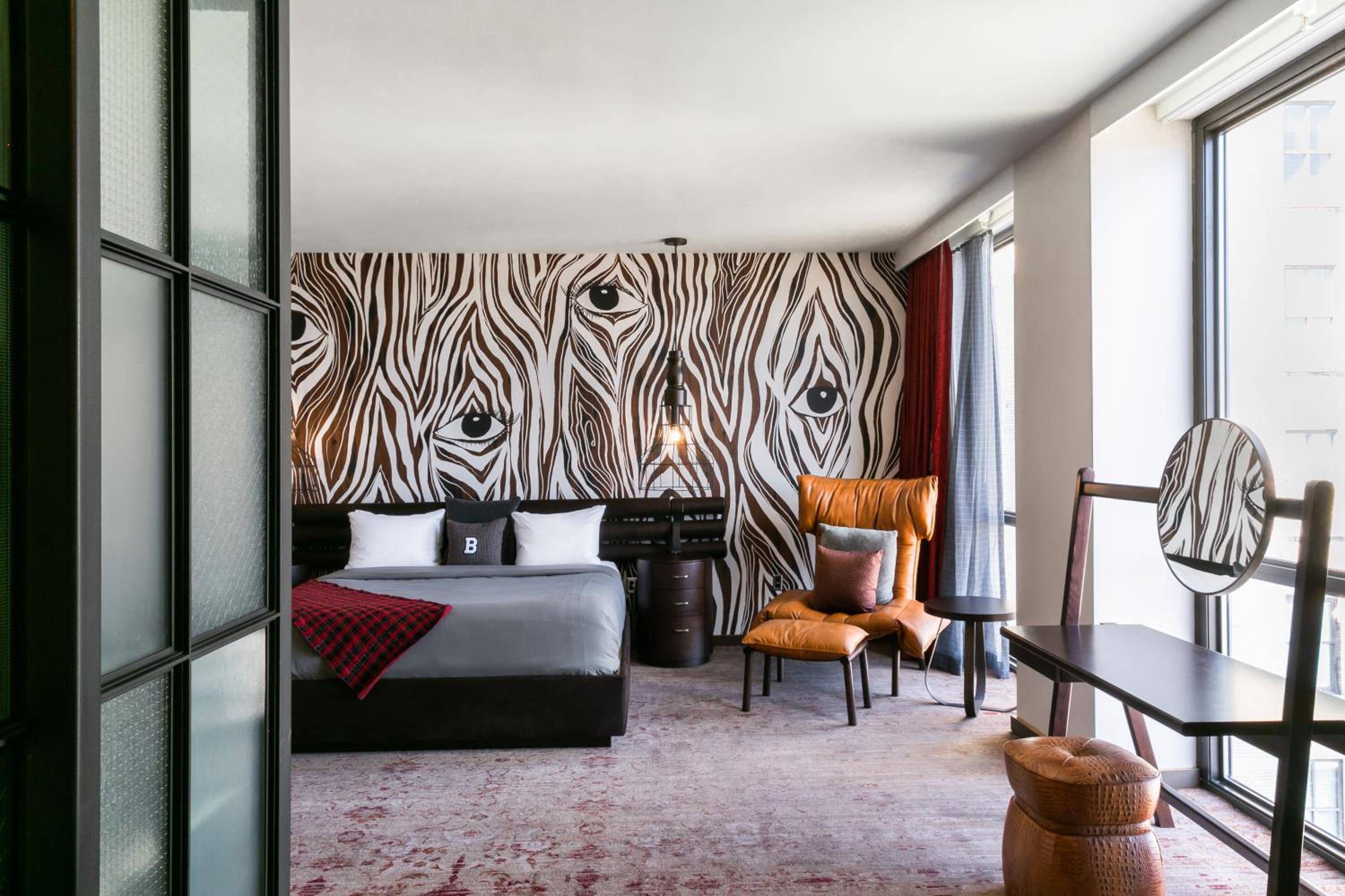 Wood-grain wallpaper creates dramatic swirls behind the king bed, while cognac leather chairs and a vintage mirror add warmth to this sophisticated Nashville retreat.