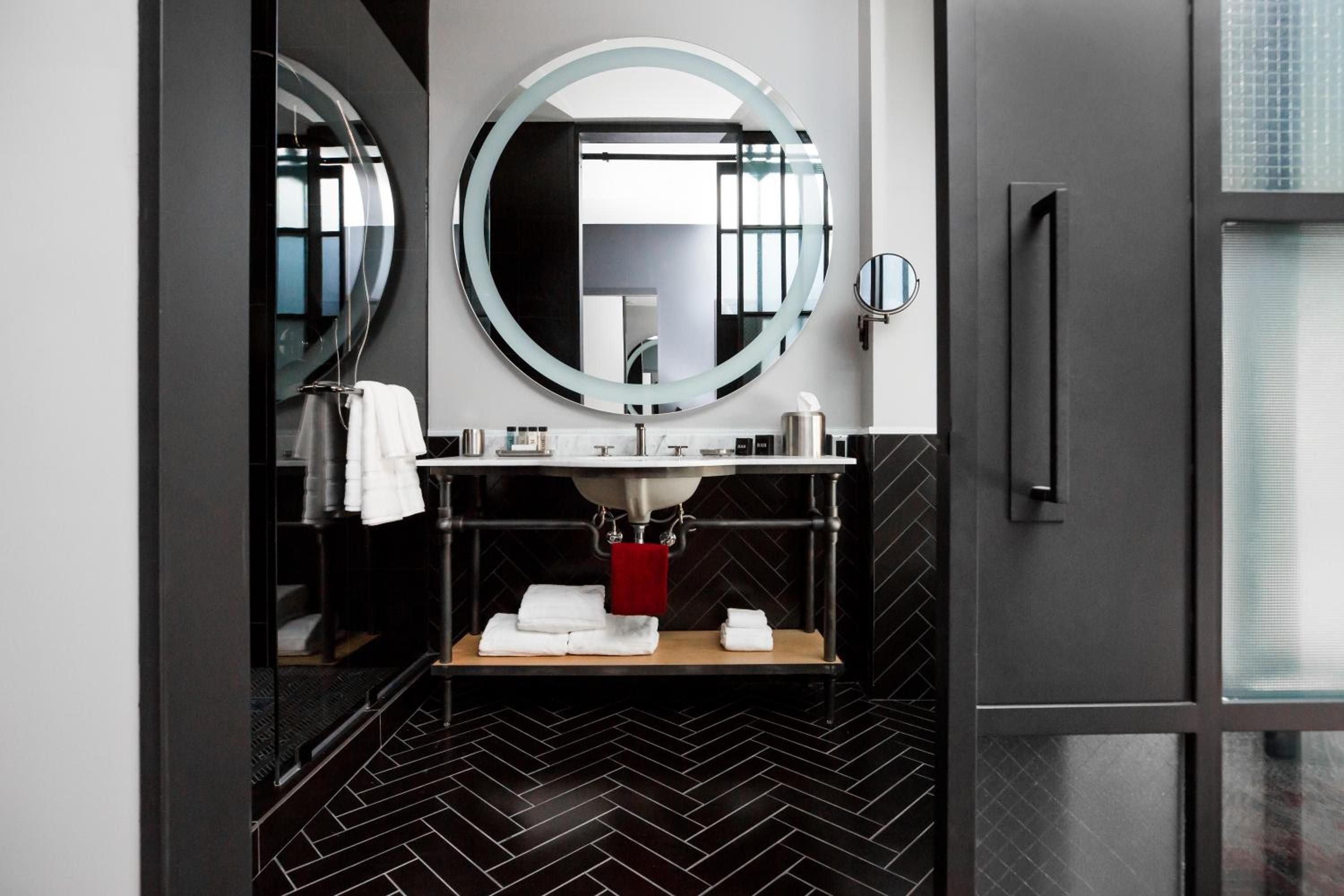 Black herringbone tiles create striking contrast against crisp white walls, while the floating marble vanity and illuminated round mirror exude modern sophistication in this thoughtfully designed guest bathroom.