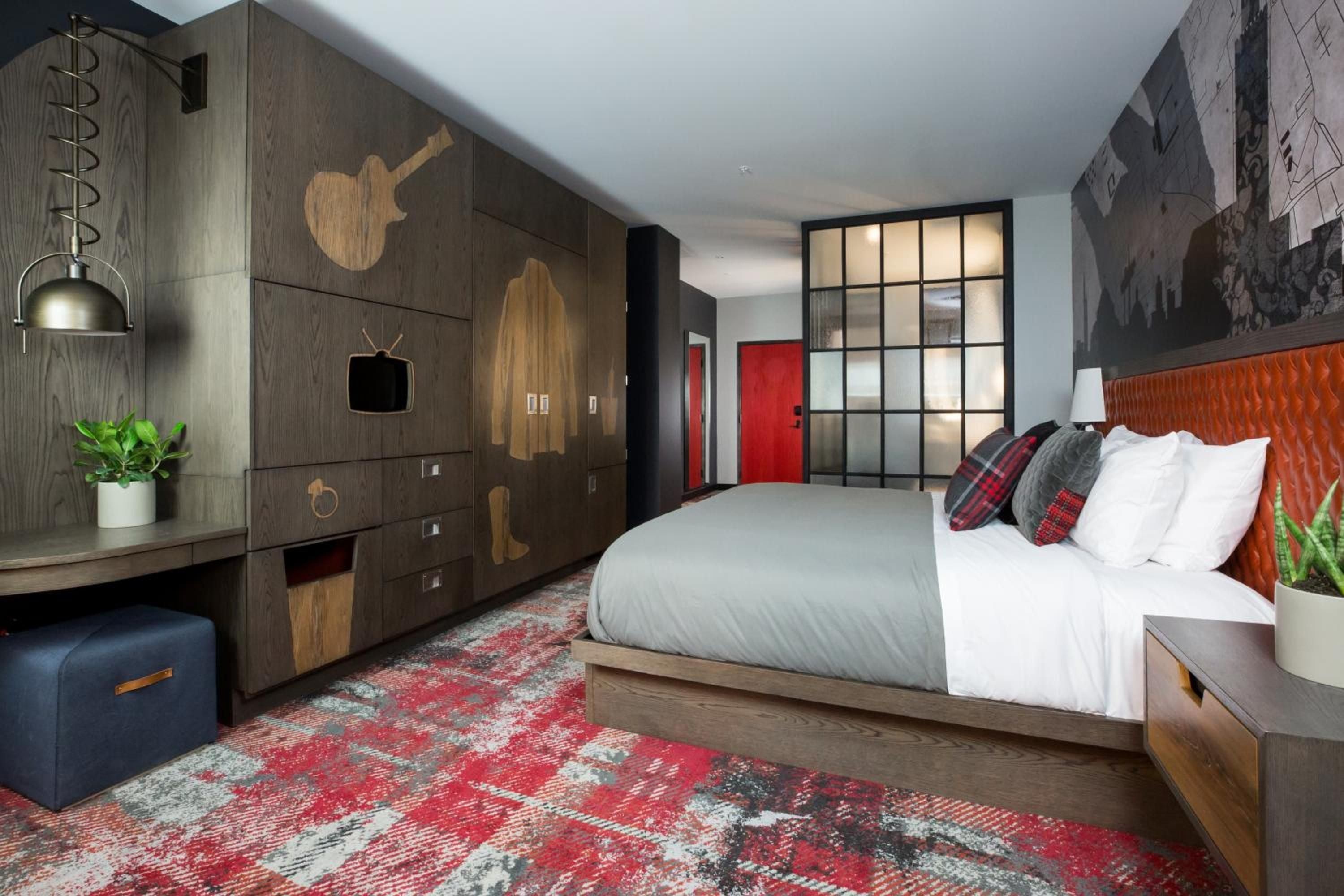 Music-themed touches like guitar silhouettes and vintage TV art transform this thoughtfully designed guest room into a rock-and-roll sanctuary with plaid accents and rich wood tones.