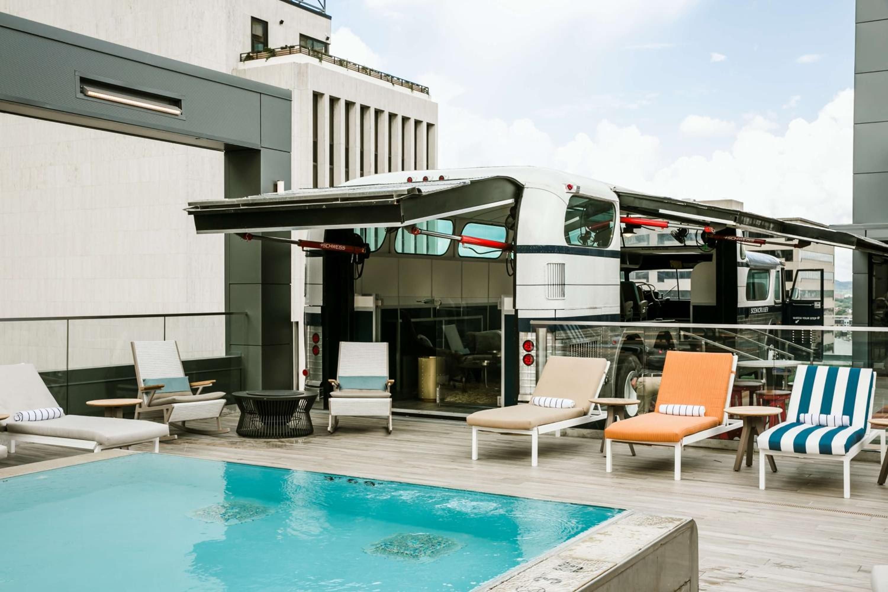 Colorful striped loungers dot the rooftop pool deck, where modern architecture frames azure waters against Nashville's urban skyline.
