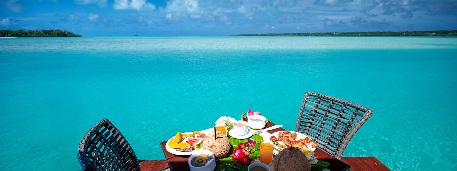 Breakfast arrives coconut-fresh at your overwater table, where turquoise lagoon waters stretch endlessly toward distant motus beneath cotton-soft clouds.