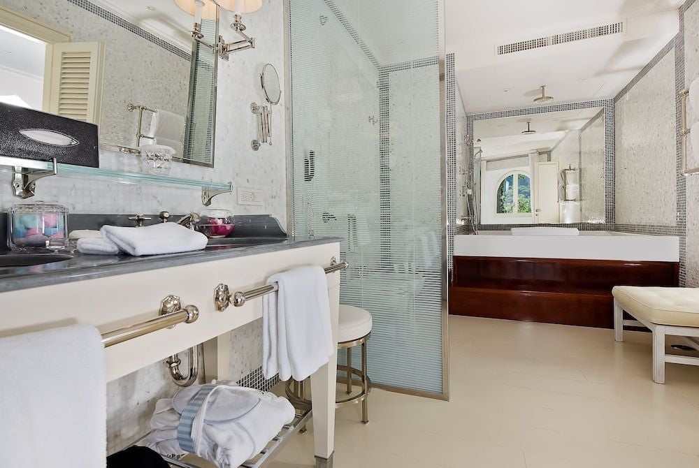 Marble surfaces gleam under soft lighting while mosaic tiles frame the glass-enclosed shower, creating an intimate spa-like sanctuary with dual vanities and polished chrome fixtures.