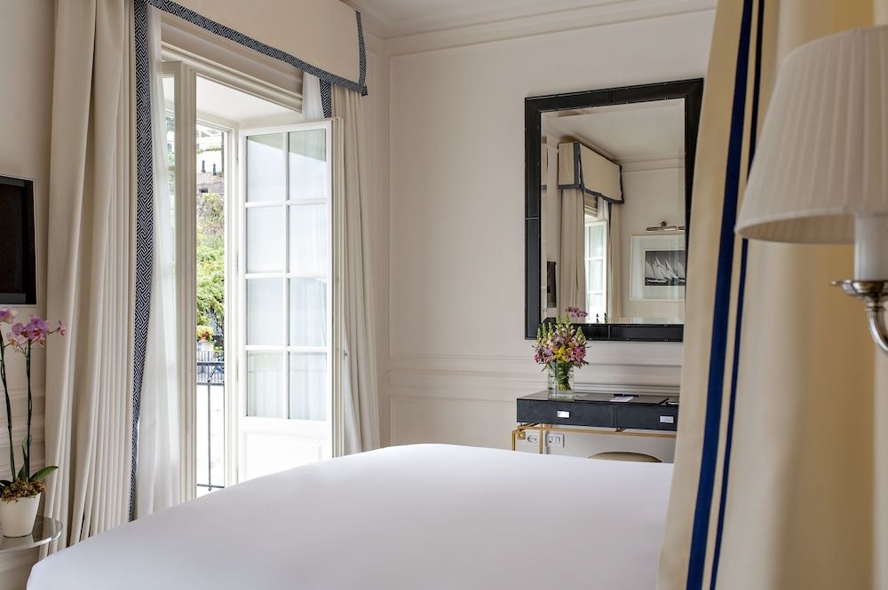 Crisp white linens and navy trim create nautical elegance in this airy suite, where French doors open to Capri's sun-drenched terraces and azure Mediterranean views.