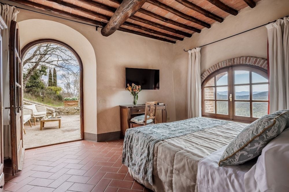 Exposed chestnut beams frame this terracotta-tiled bedroom where arched doorways open to sun-drenched terraces overlooking Chianti's rolling vineyard landscape.