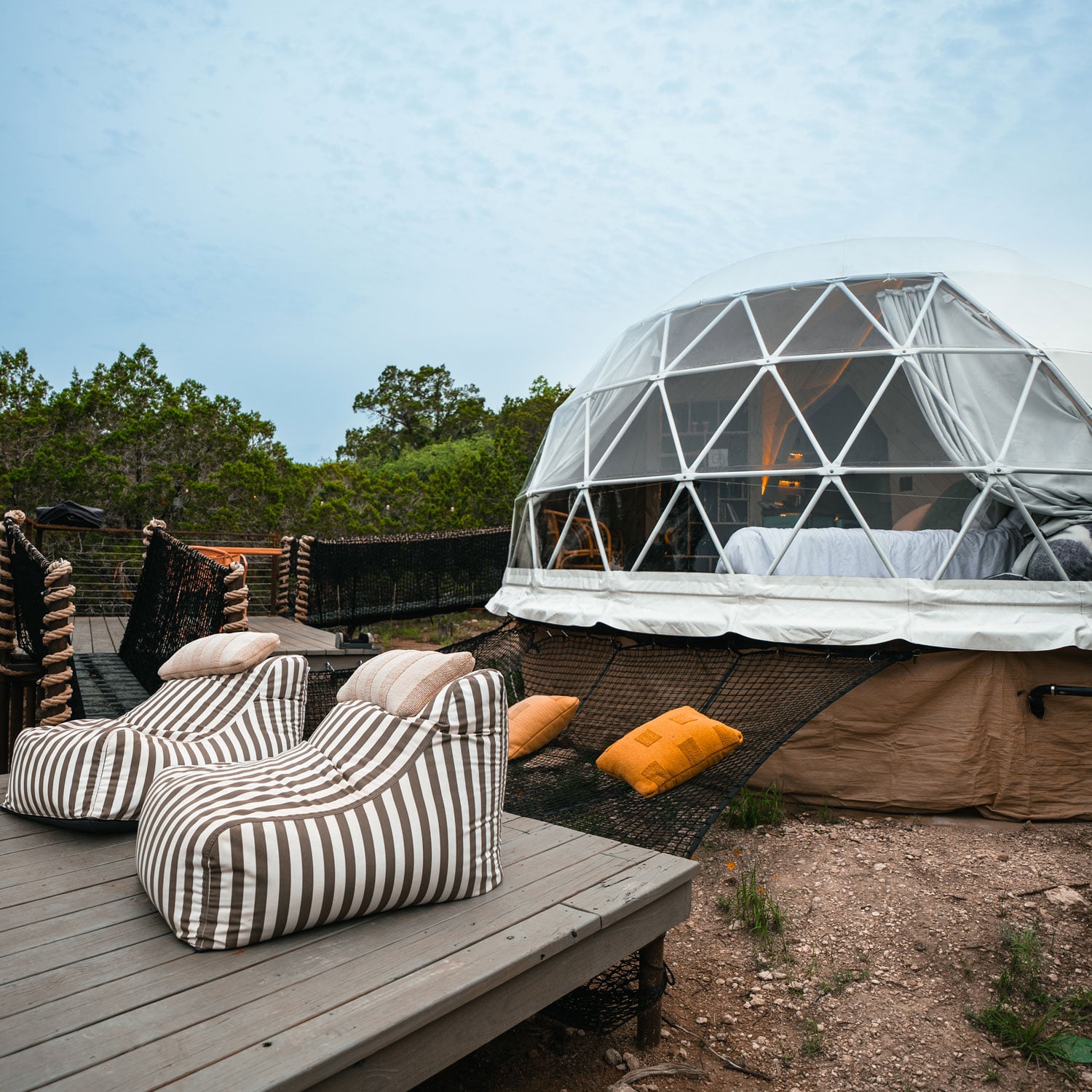 Geodesic glamping domes offer stargazing luxury with crisp white linens visible through transparent panels, while striped lounge chairs dot weathered wooden decking.