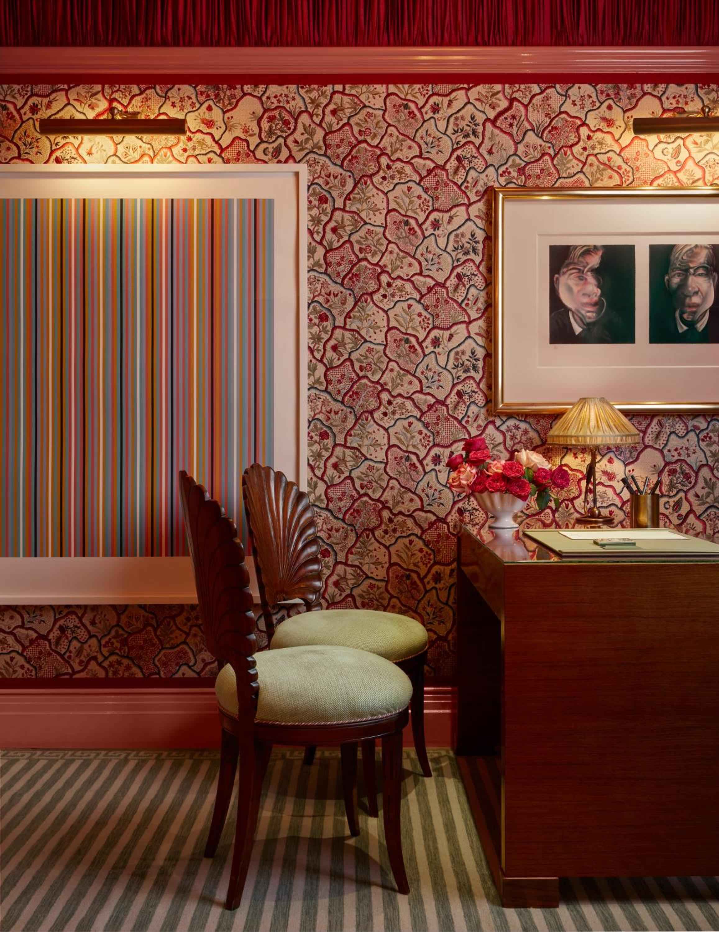 Ornate crimson wallpaper frames vibrant contemporary art in an intimate writing nook, where carved wooden chairs invite guests to linger over correspondence and cocktails.