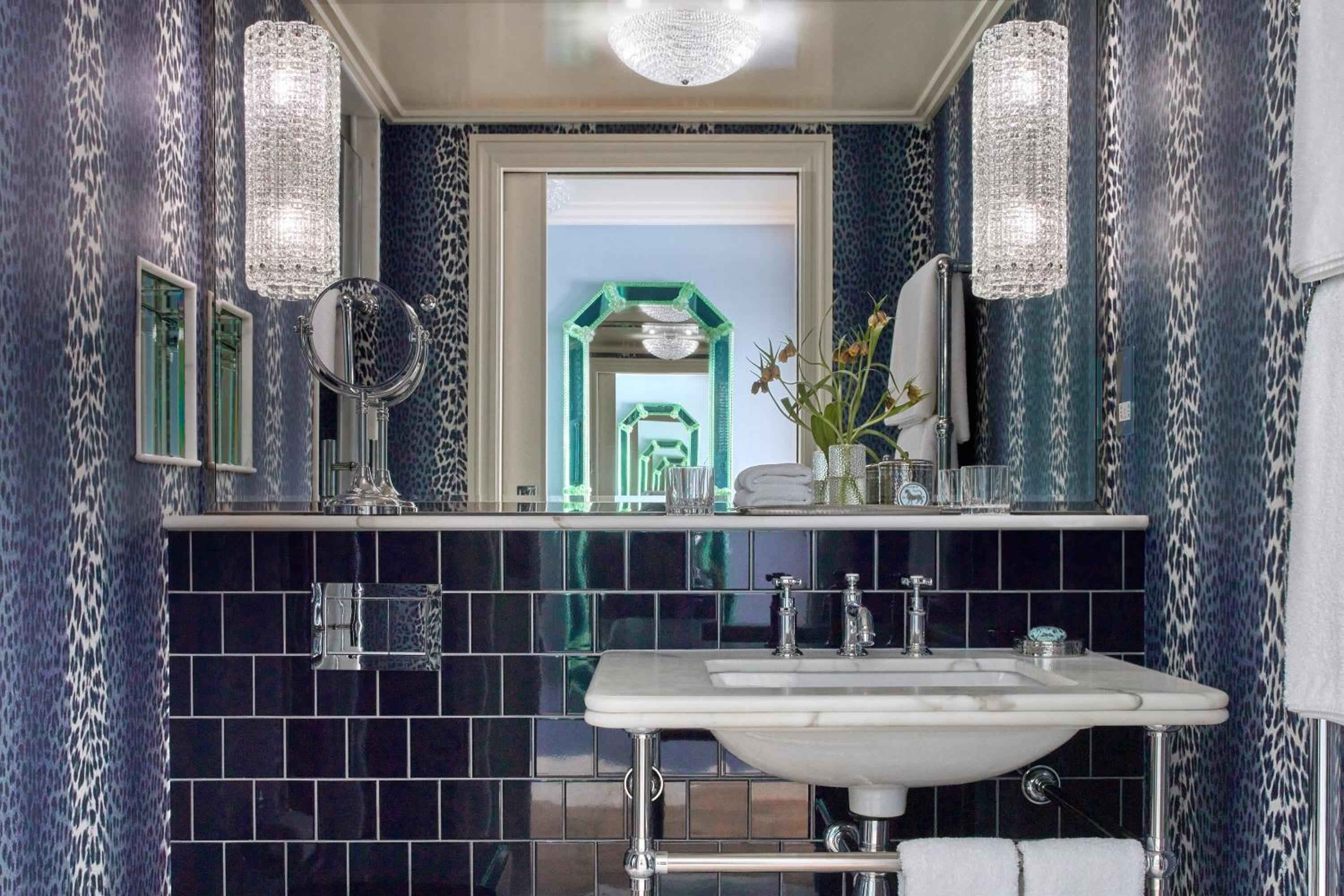 Leopard-print wallpaper and emerald green mirrors create a boldly glamorous powder room where crystal sconces cast flattering light over vintage-inspired fixtures.