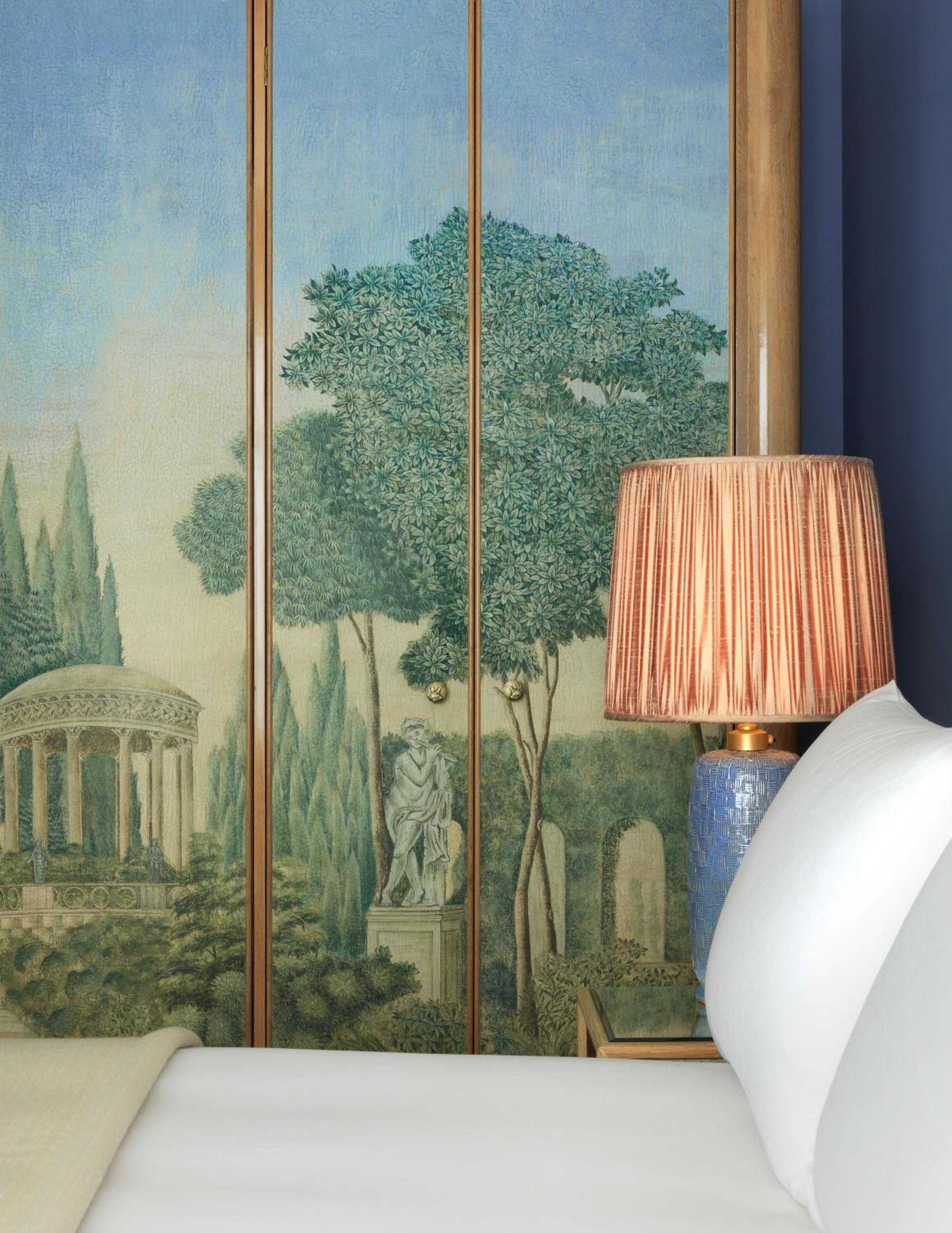 Hand-painted pastoral murals frame the bedside, where coral-hued lampshades cast warm light against classical scenes of gardens and temples.