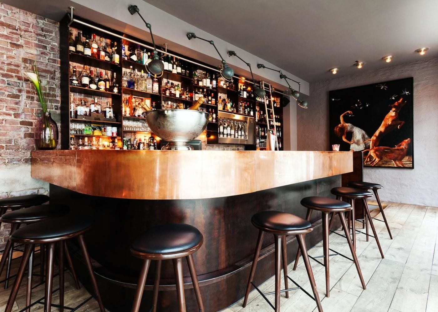 Copper gleams against exposed brick at this intimate bar, where mid-century stools invite lingering over craft cocktails beneath moody track lighting.
