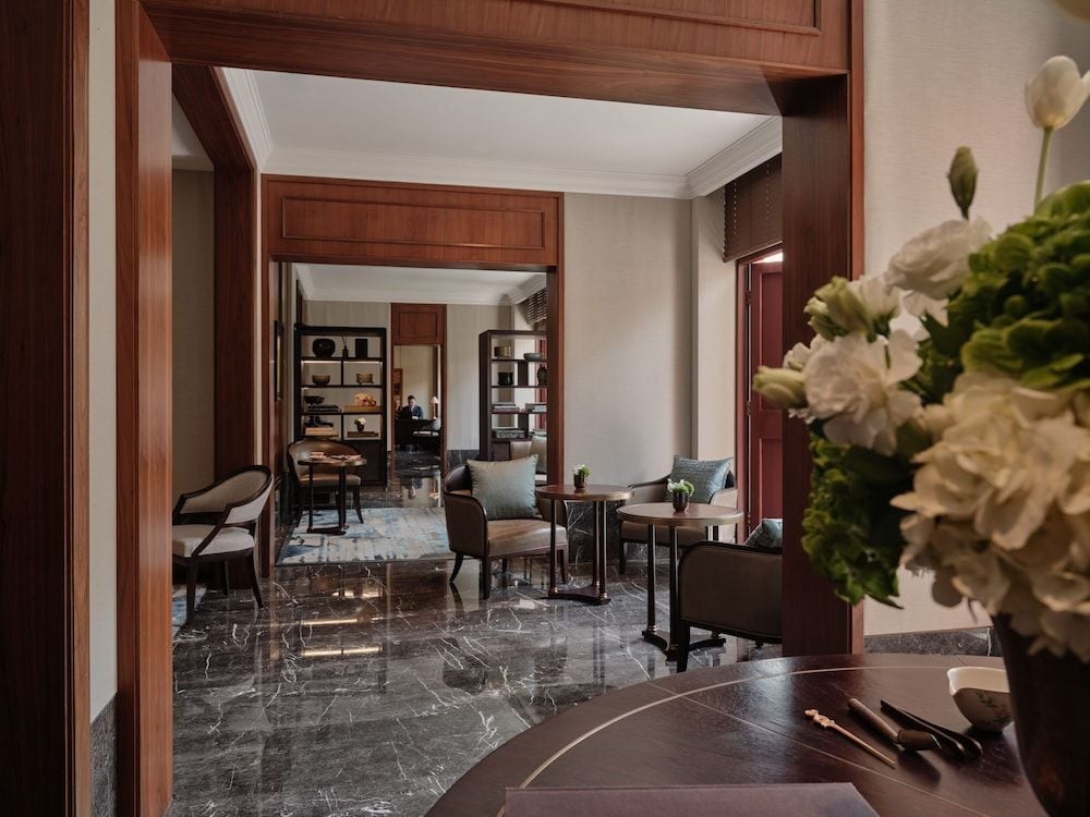 Rich walnut frames create intimate alcoves throughout the lobby, where plush seating and fresh white blooms invite lingering conversations over afternoon tea.