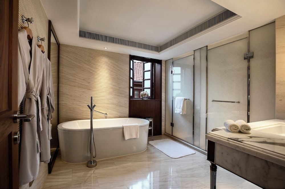 Marble surfaces gleam under soft lighting while a freestanding soaking tub anchors this spa-like sanctuary, complete with glass-enclosed shower and plush robes awaiting.