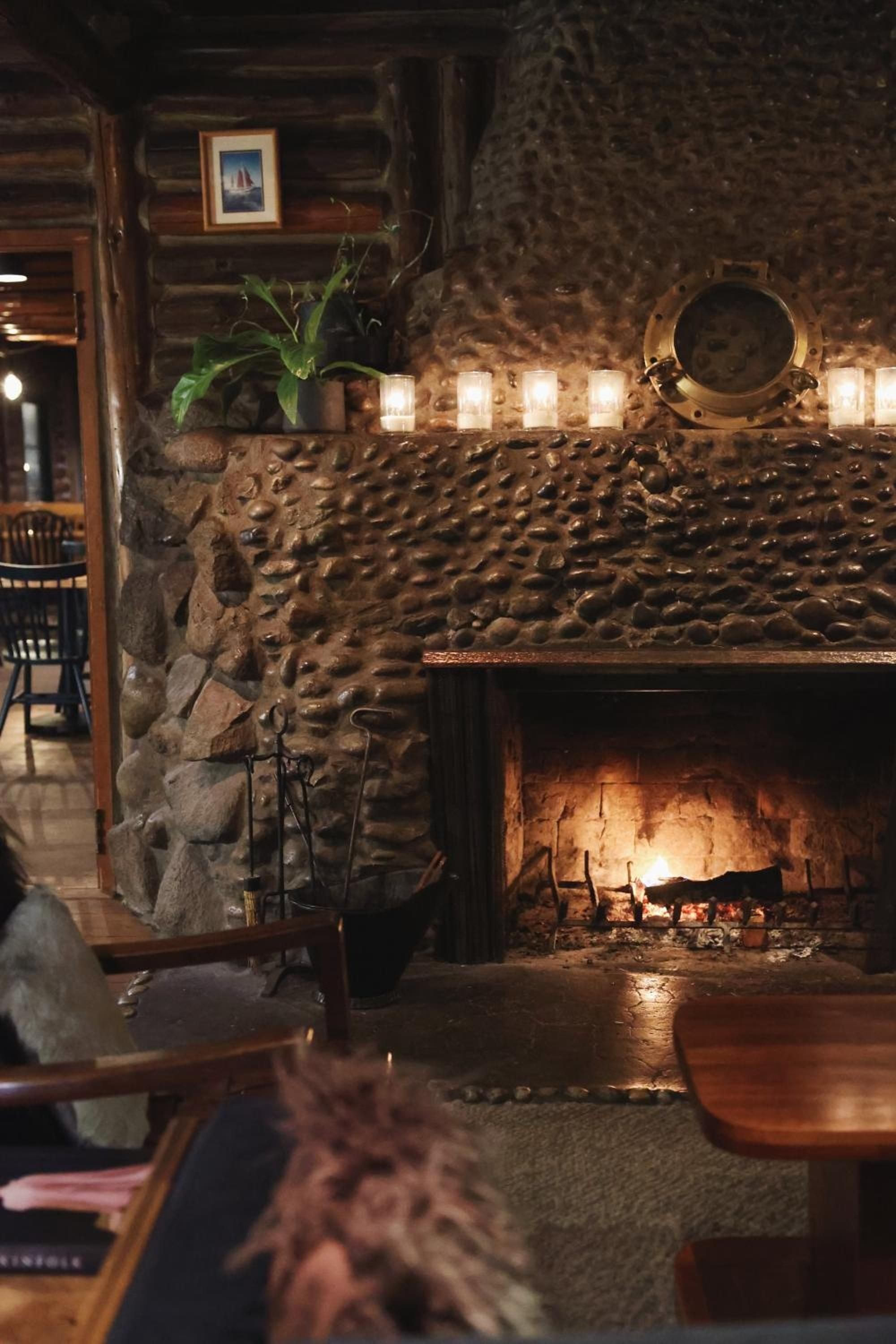 Cobblestone fireplace walls glow with candlelight while copper vessels and maritime artifacts create an intimate tavern atmosphere steeped in Pacific Northwest maritime history.