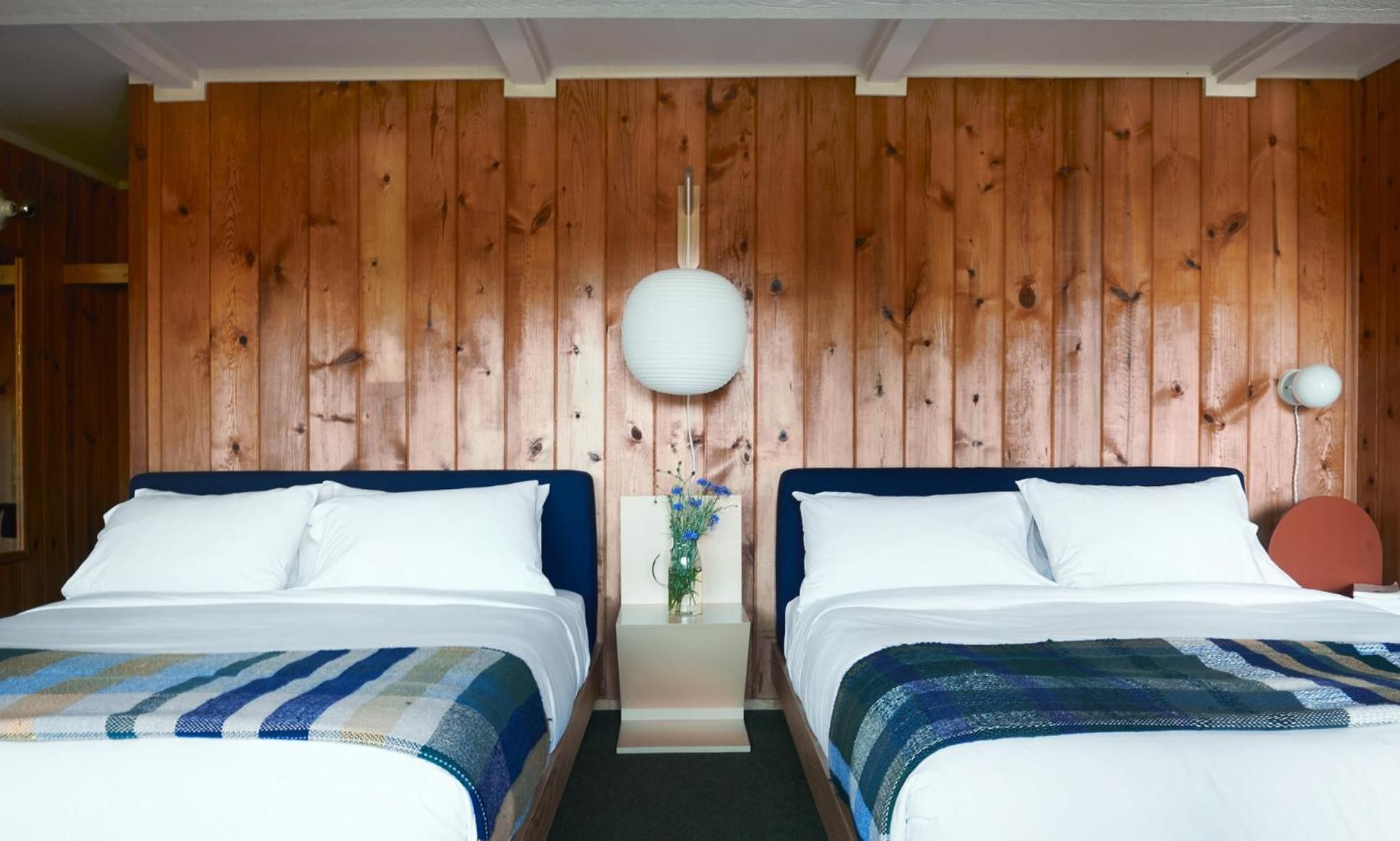 Twin beds with navy headboards and striped throws create a nautical haven against warm cedar planking, where paper lanterns cast gentle shadows in this intimate guest room.