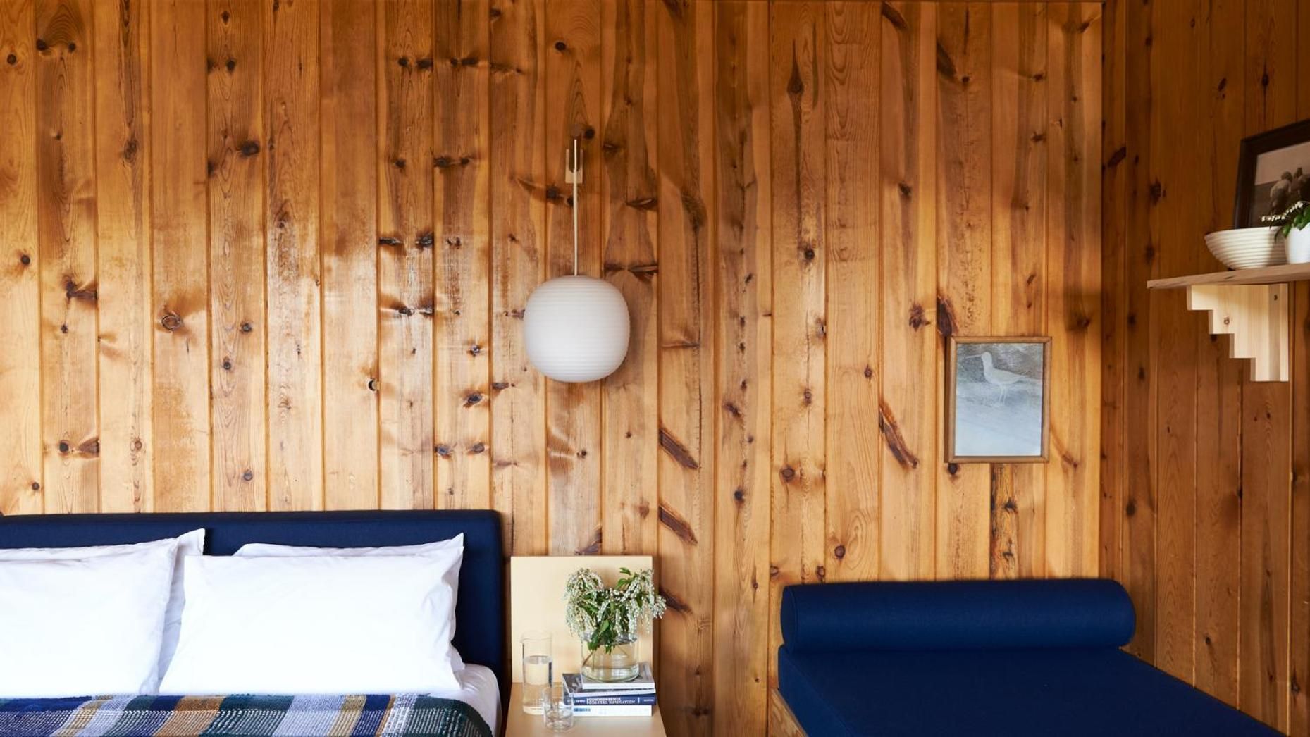 Knotty pine walls embrace a navy-upholstered bed and built-in banquette, where pendant lighting casts warm shadows across this cozy Pacific Northwest retreat.