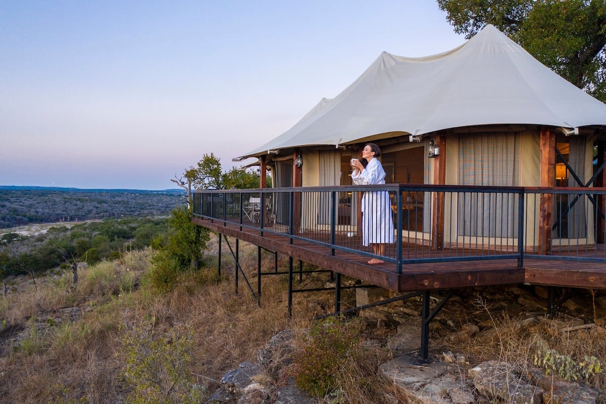 Safari-style canvas tents perch on elevated wooden decks, where guests sip evening drinks while surveying the wild Texas Hill Country stretching endlessly below.