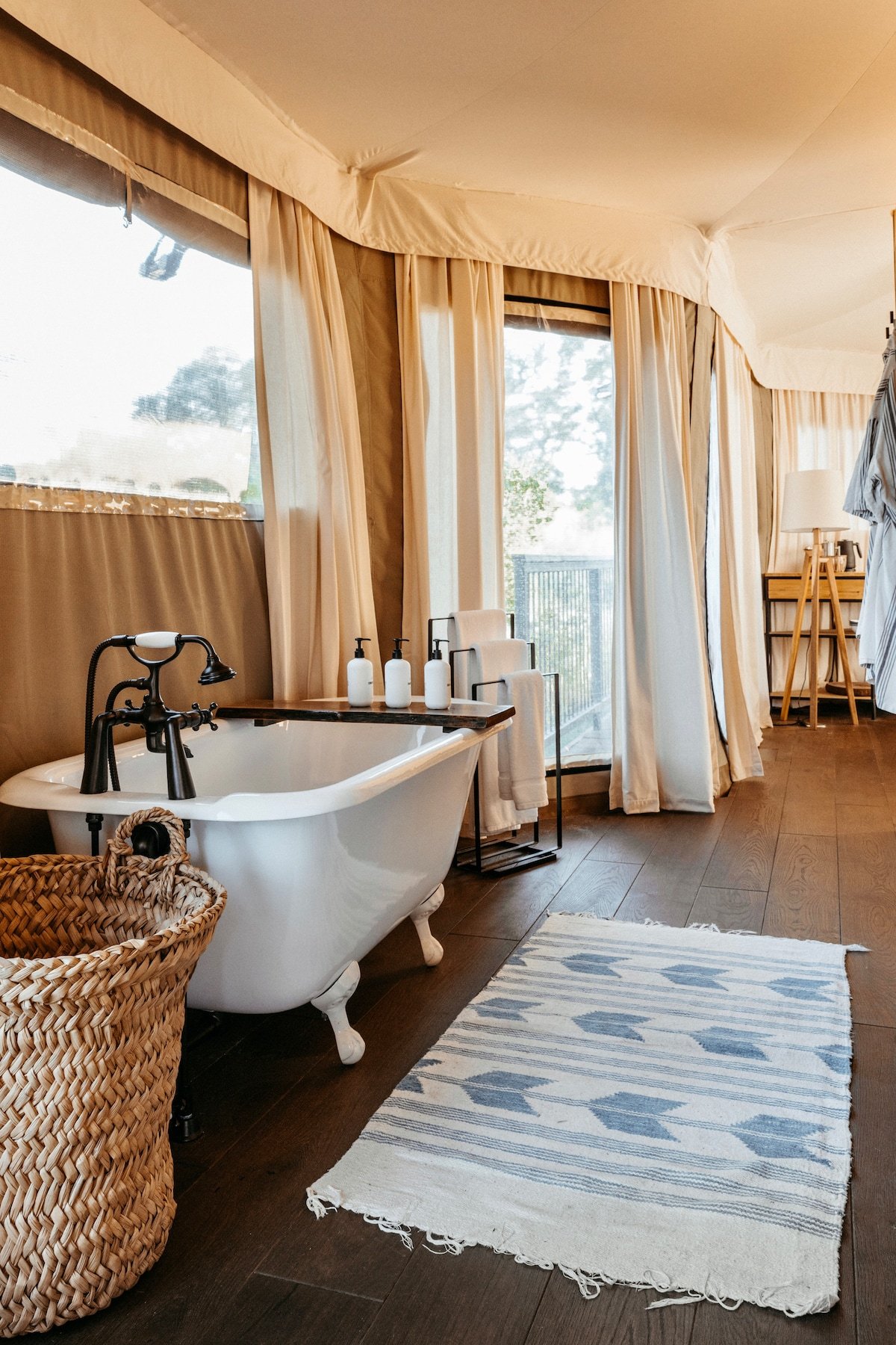 Natural light filters through canvas walls onto the clawfoot tub, where woven baskets and organic linens create a safari-meets-spa sanctuary.