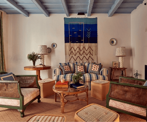 Exposed wooden beams frame a cozy seating area where rattan furniture, vibrant textiles, and indigo wall art create an effortlessly sophisticated Andalusian retreat.