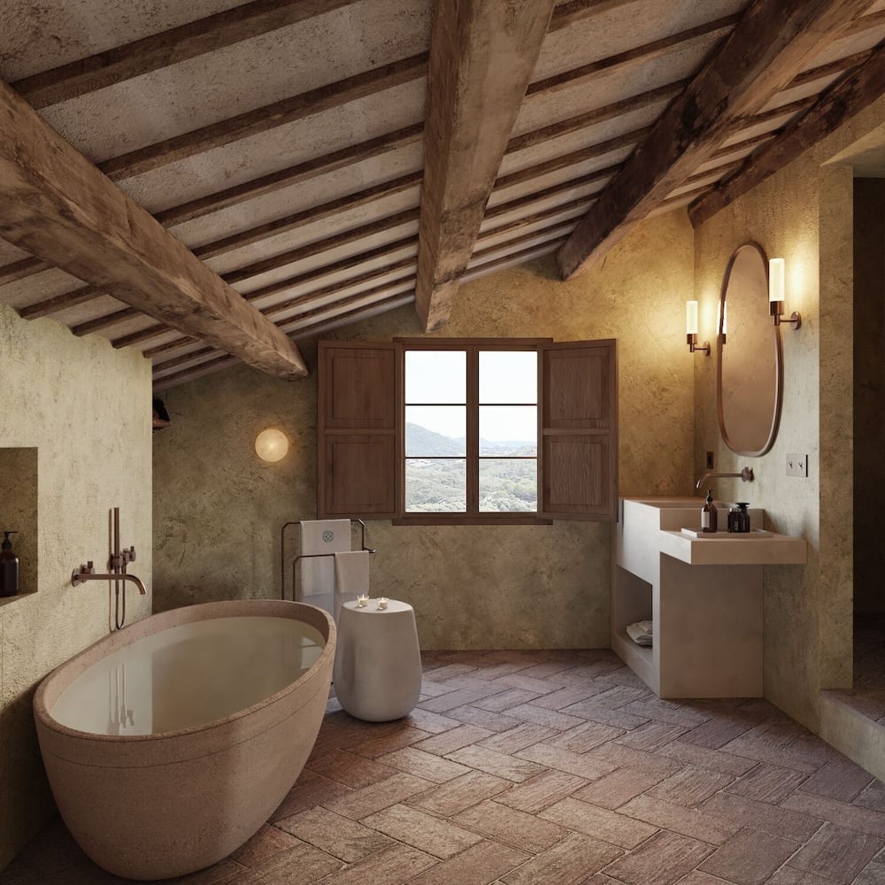 Exposed timber beams frame this rustic-luxe bathroom sanctuary, where a curved stone soaking tub and raw plaster walls create an intimate countryside retreat.