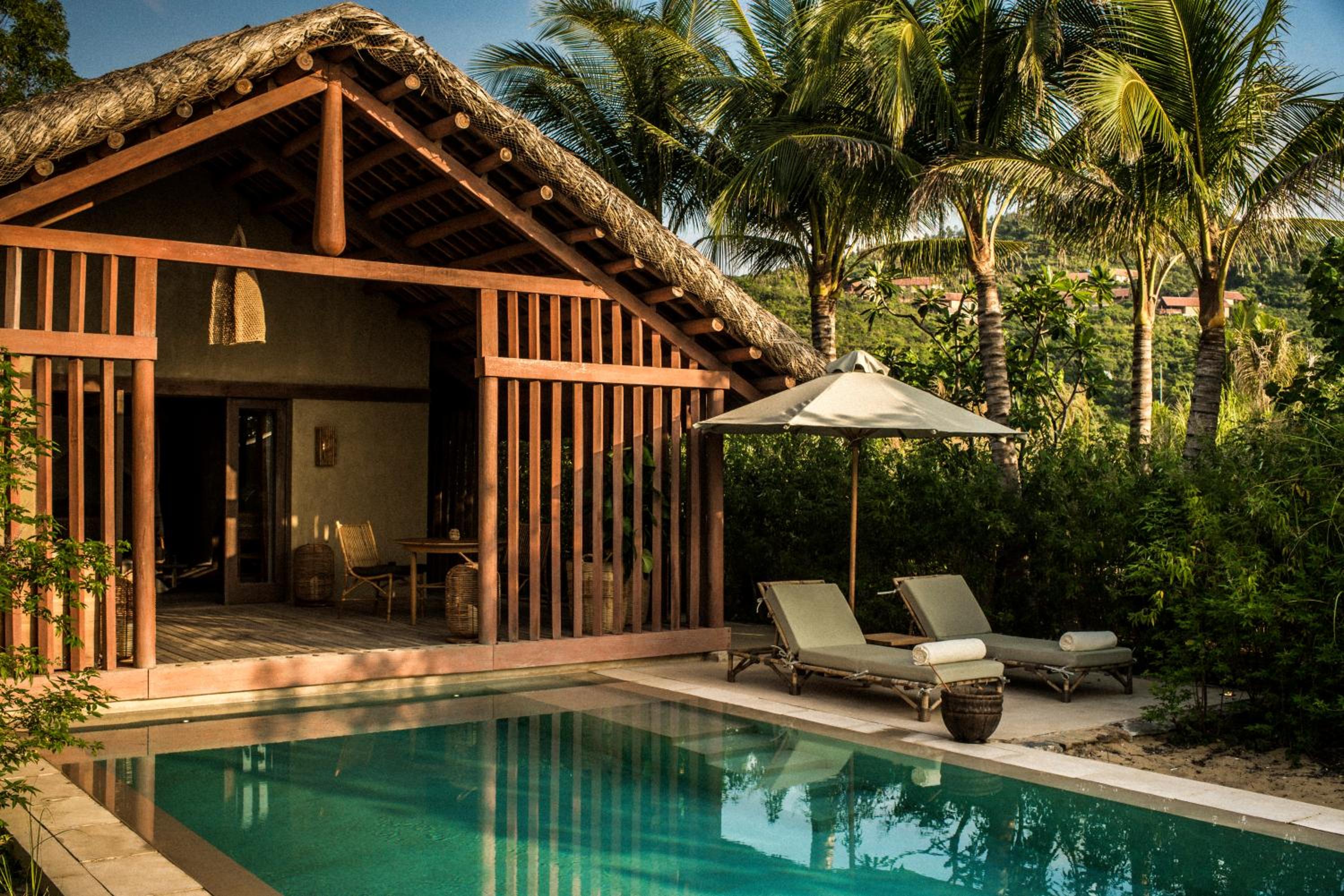 Thatched pavilion architecture meets turquoise infinity waters, where woven lounge chairs beckon beneath swaying palms and golden afternoon light filters through tropical foliage.