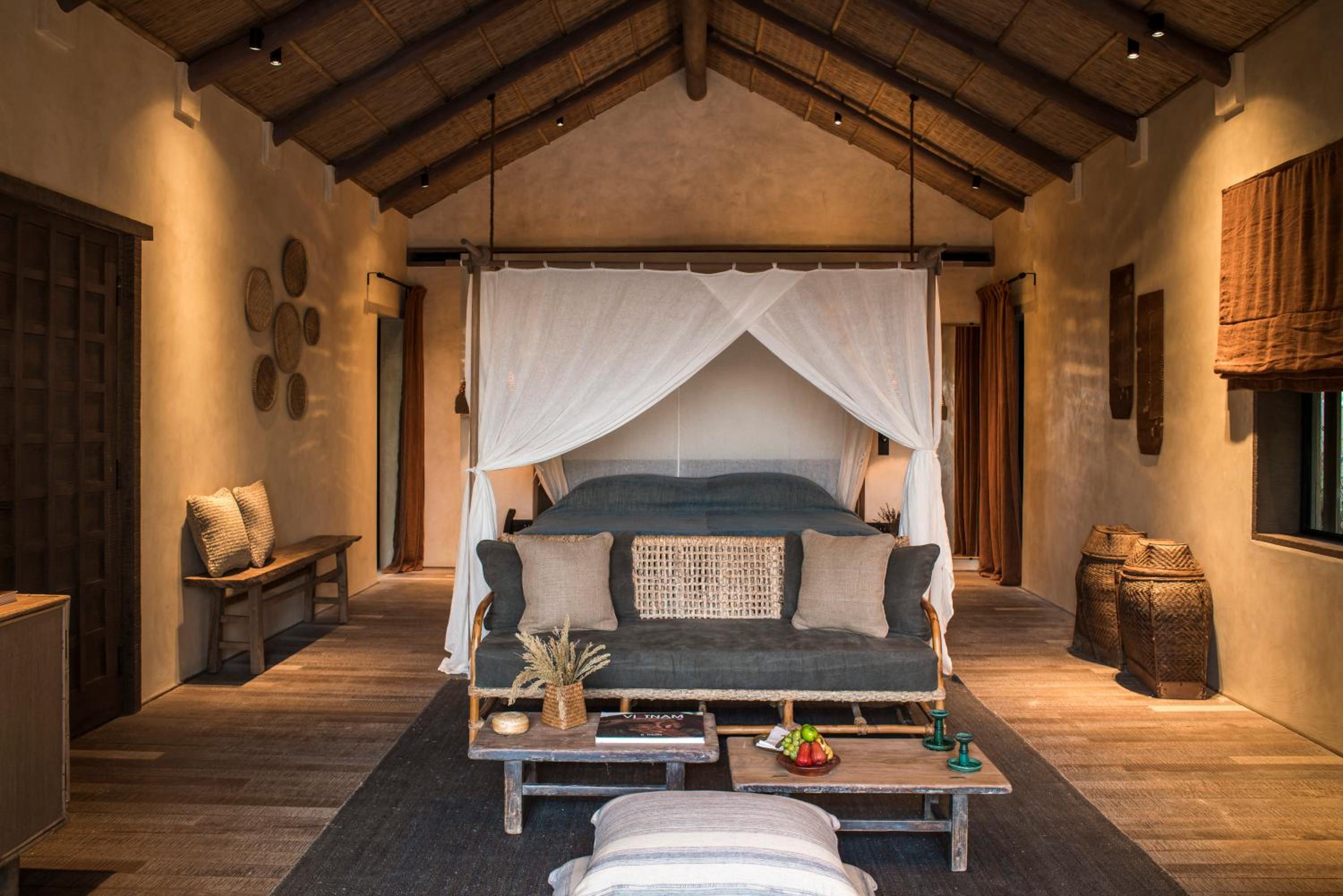 Woven baskets and weathered wood create an intimate sanctuary where mosquito netting frames the four-poster bed beneath rustic bamboo beams.