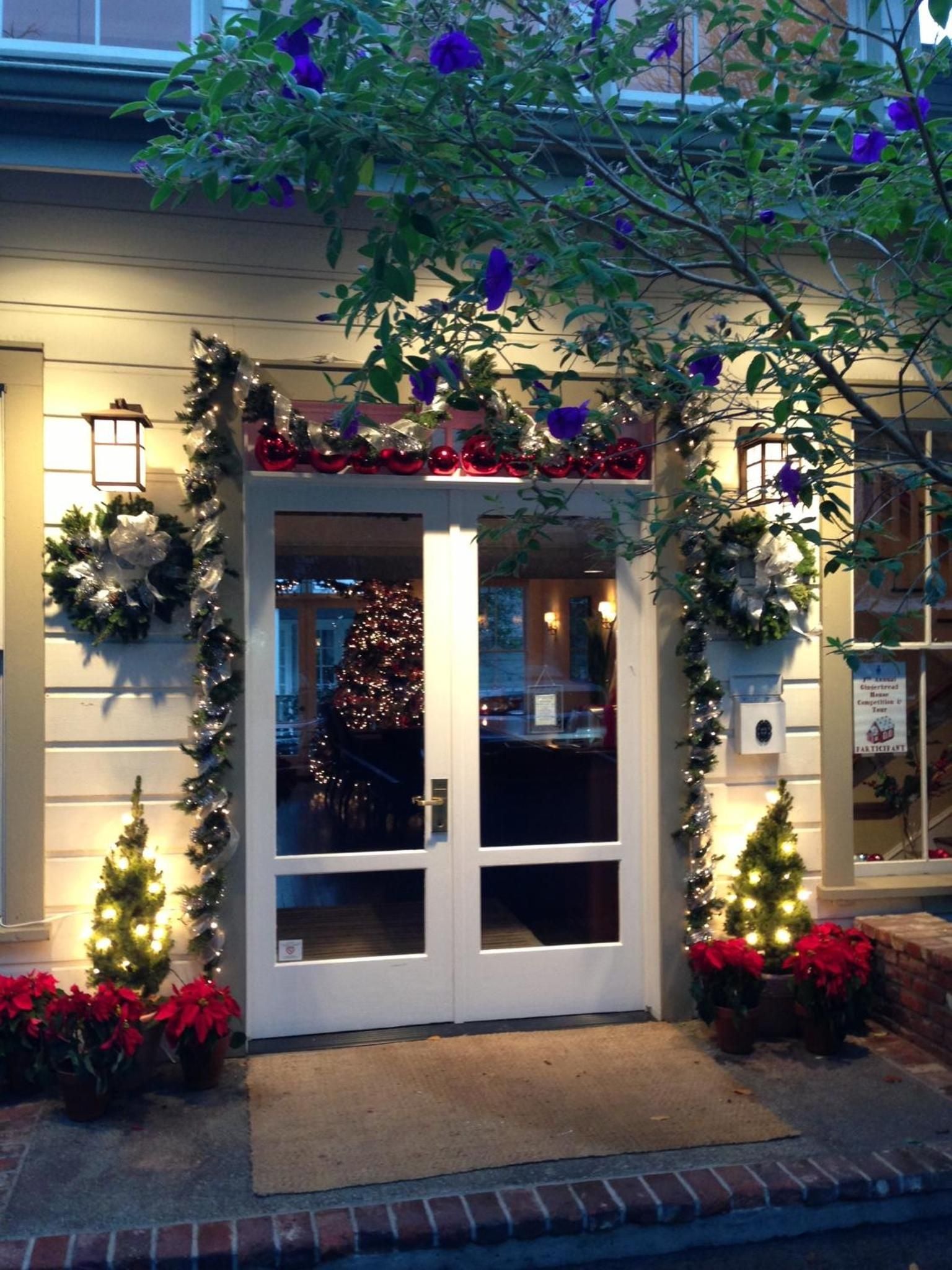 Festive garland and twinkling lights frame the lodge's welcoming entrance, where red poinsettias and miniature Christmas trees create an enchanting holiday tableau against warm golden walls.