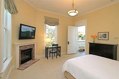 Sunlight streams through elegant windows into this sophisticated guest room, where a marble fireplace and French doors create an intimate retreat with classic California charm.