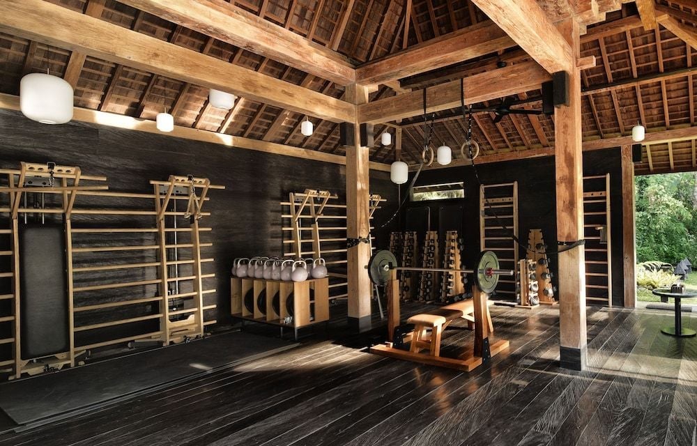 Traditional Balinese timber frames soar above this wellness sanctuary, where Swedish wall bars and suspension rings blend seamlessly with warm wood and filtered natural light.