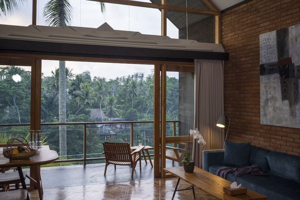 Warm brick walls and teak furnishings frame sweeping jungle vistas from this elevated pavilion, where tropical breezes drift through floor-to-ceiling windows above Ubud's emerald canopy.