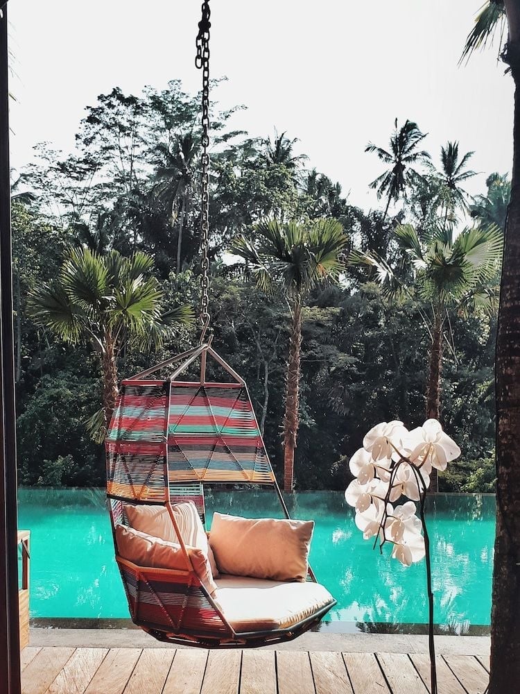 Suspended wicker cocoons invite lingering poolside moments, where tropical palms frame turquoise waters and orchid stems dance in Bali's golden afternoon light.