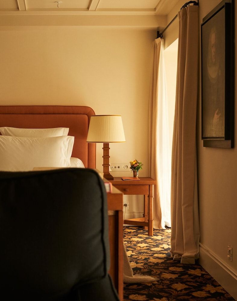 Warm amber light filters through linen curtains, illuminating the handcrafted wooden headboard and vintage-inspired furnishings that define each thoughtfully appointed guest room.