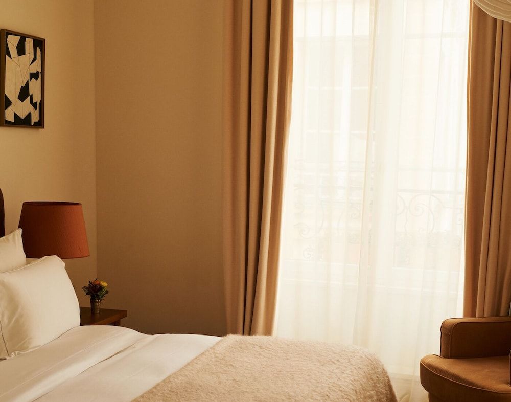 Warm amber light filters through honey-toned curtains, illuminating crisp white linens and burnt orange accents that create an intimate sanctuary of understated elegance.