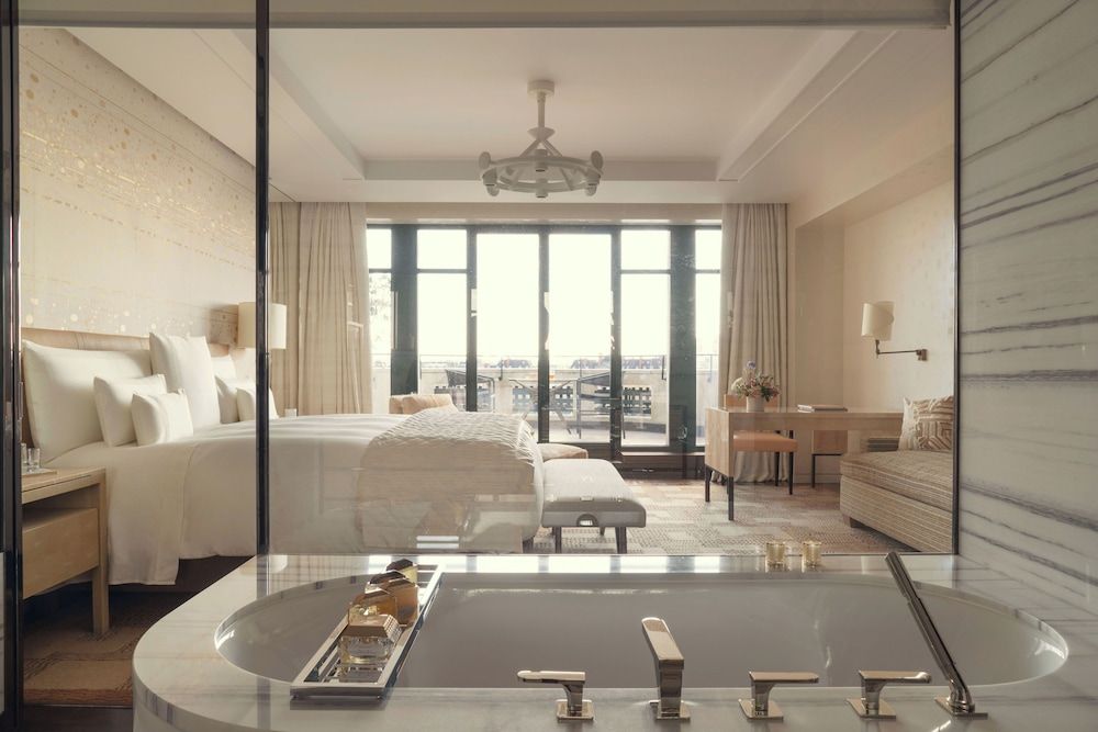Marble and warm wood create an intimate sanctuary where the oversized soaking tub offers front-row seats to Paris's rooftops through floor-to-ceiling windows.