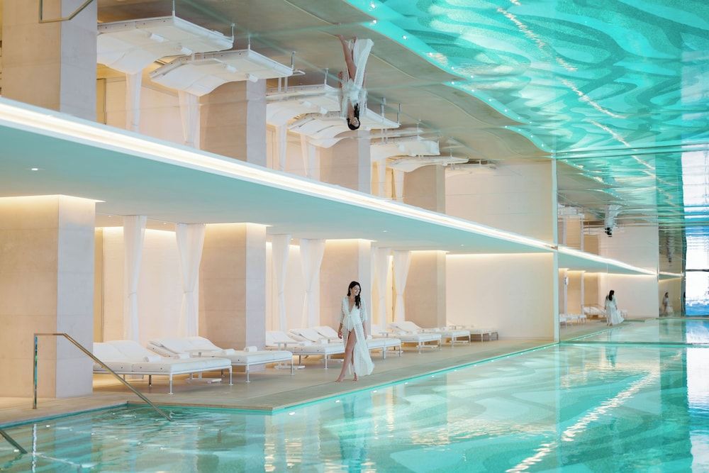 Turquoise water reflects dancing light patterns across pristine white loungers in this ethereal underground sanctuary, where minimalist columns frame moments of pure serenity.