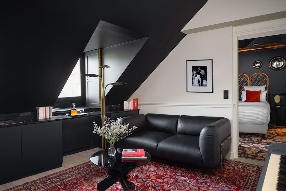 Dramatic black ceilings meet crisp white walls in this sophisticated suite, where Persian rugs warm dark leather seating and golden light spills through dormer windows.