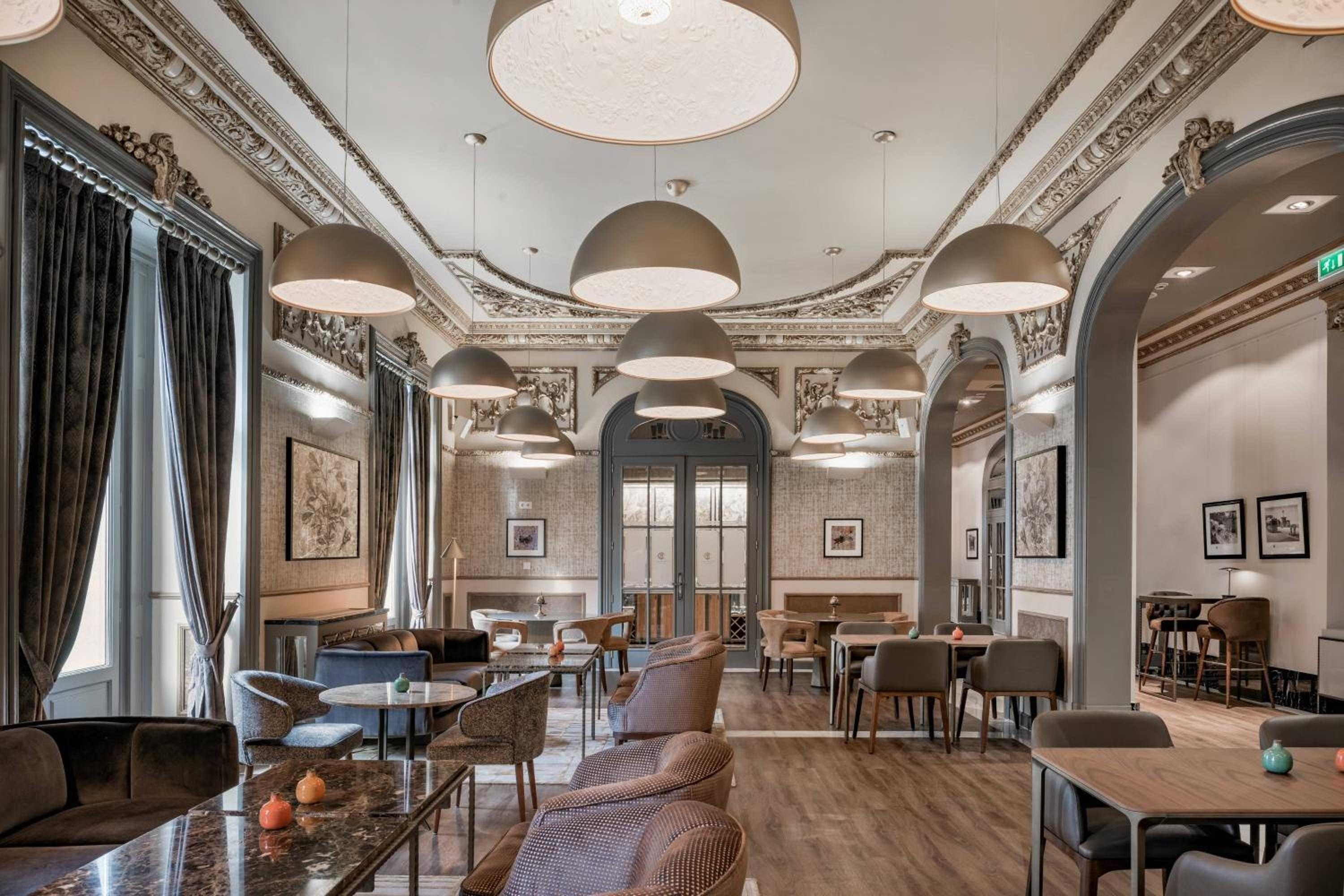 Ornate moldings and contemporary pendant lights create striking contrast in this grand dining space, where classical architecture meets modern comfort beneath soaring decorated ceilings.