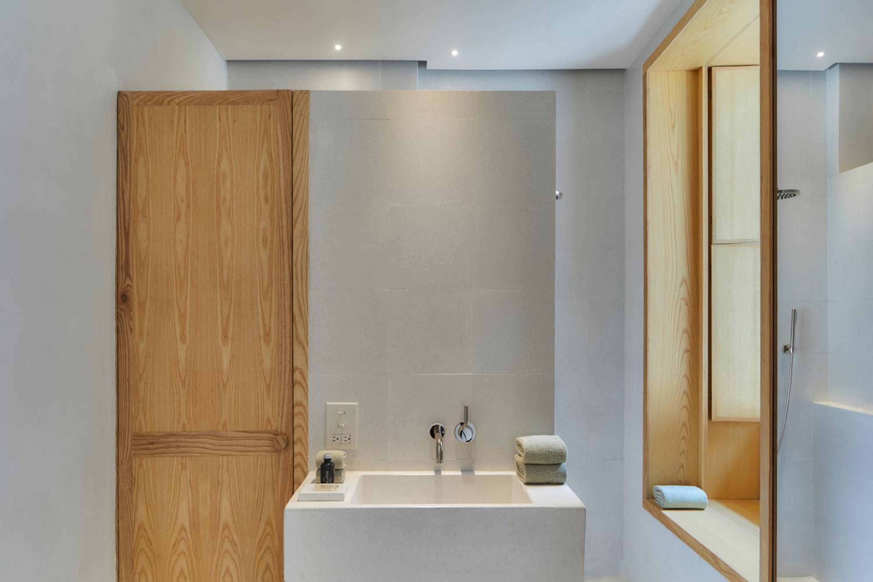 Warm oak cabinetry and sleek concrete surfaces create a sophisticated spa-like sanctuary where natural wood grains soften minimalist lines.