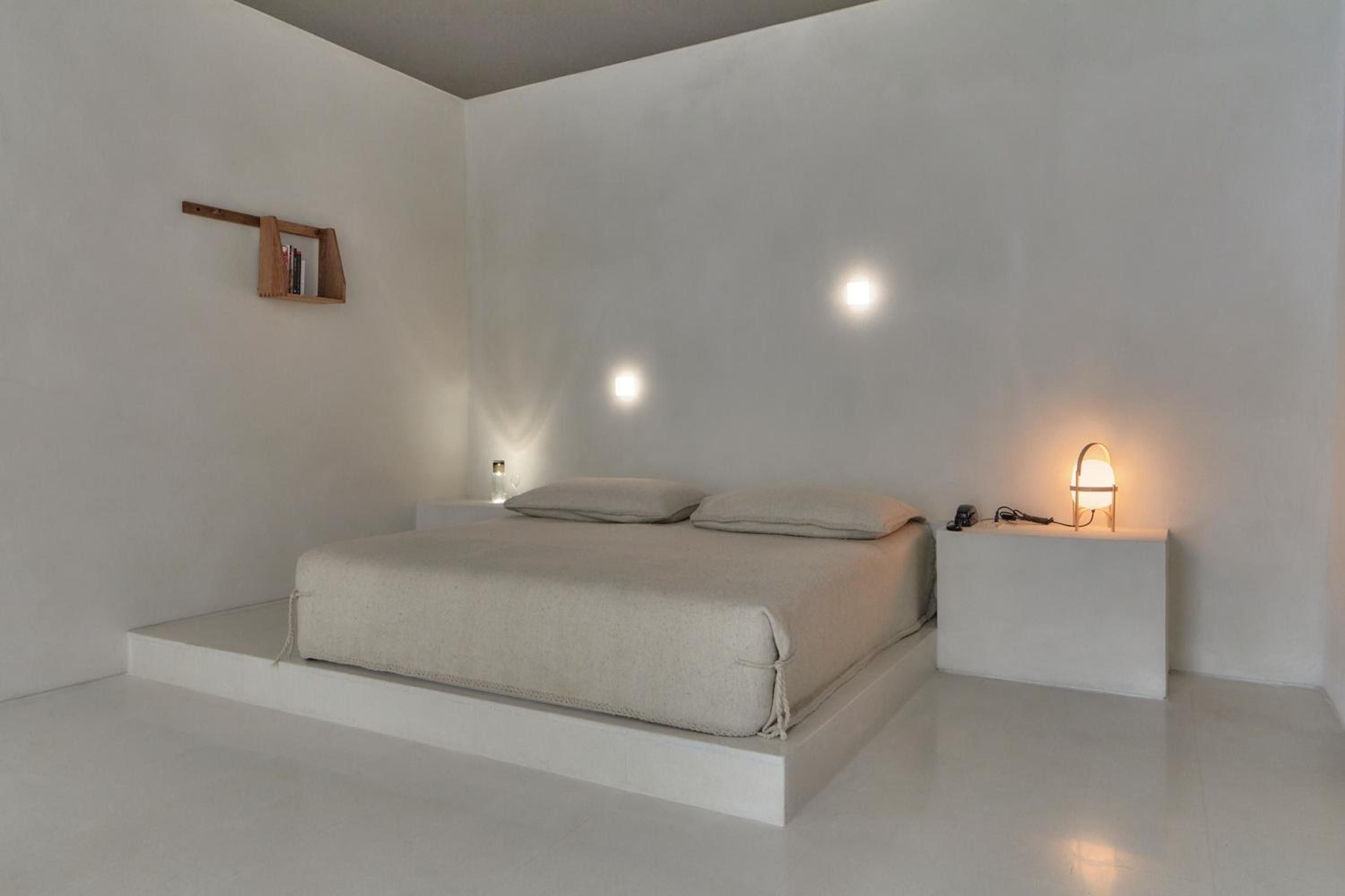Minimalist luxury defines this pristine suite where built-in platforms create a floating bed effect, while warm amber lighting softly illuminates the sculptural white architecture.