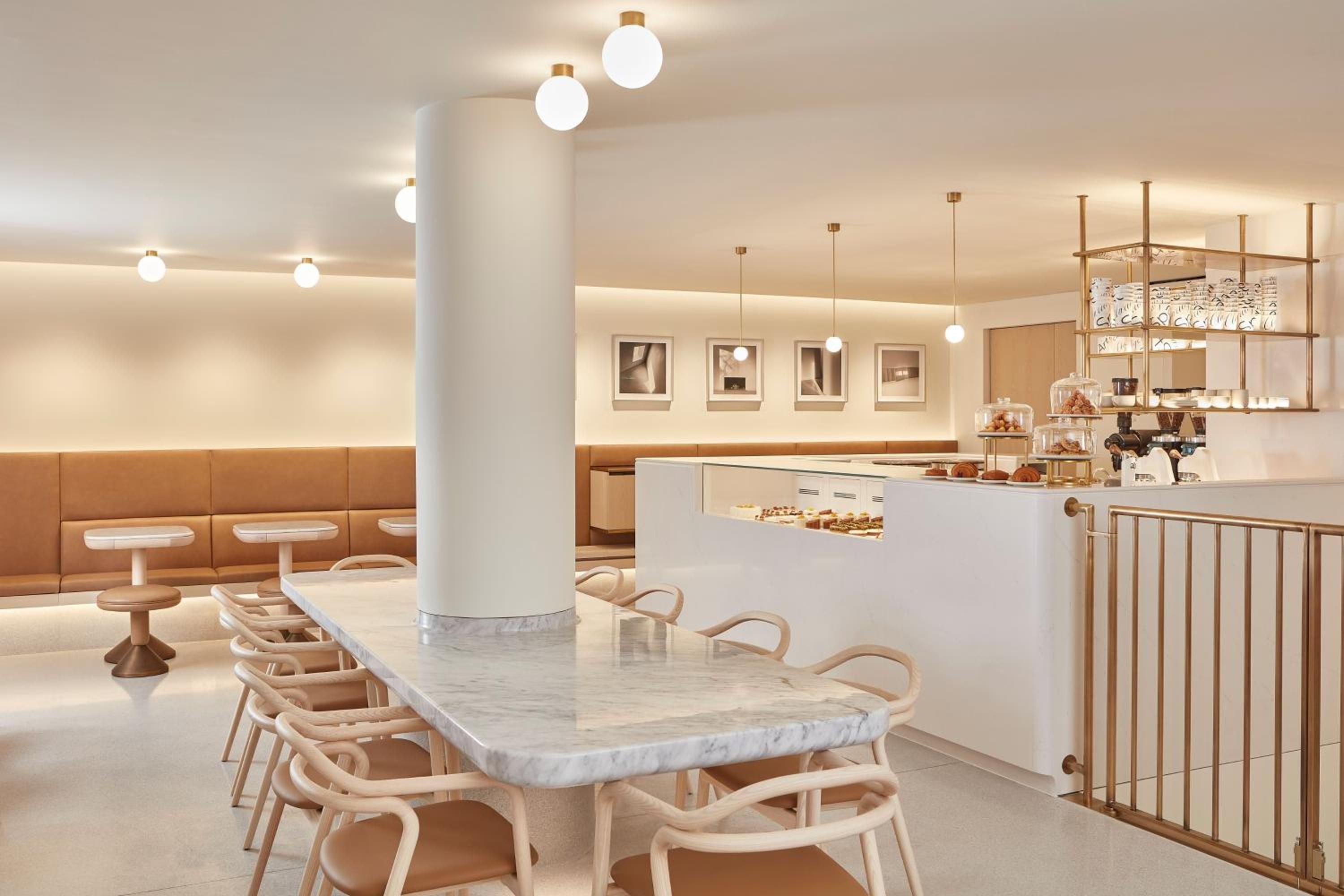 Warm oak banquettes and honey-hued lighting create an intimate pastry counter setting where Carrara marble meets brass details in sophisticated harmony.