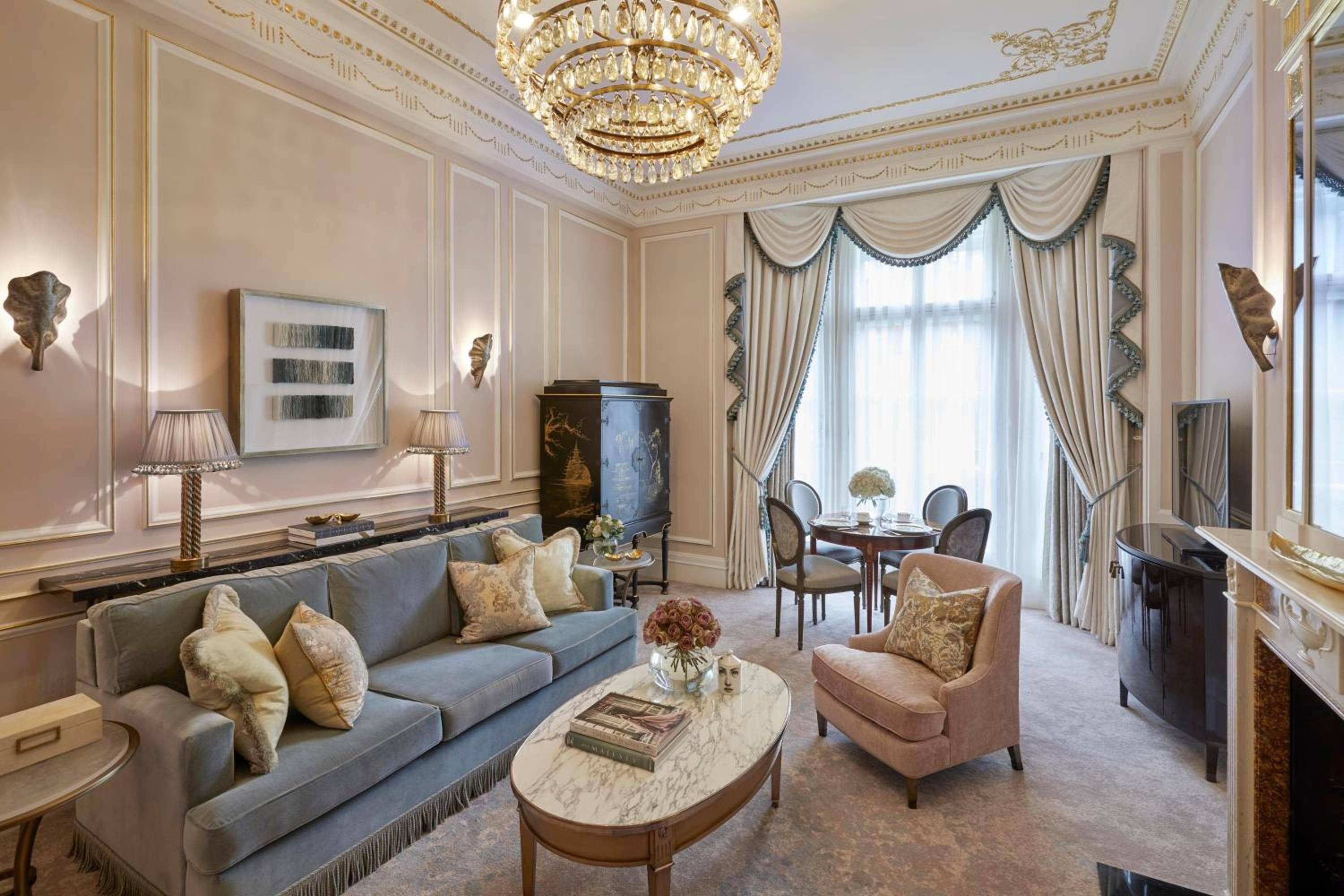 Ornate crown molding and crystal chandeliers frame this palatial suite, where powder-blue velvet meets marble and gilded details in quintessentially British luxury.