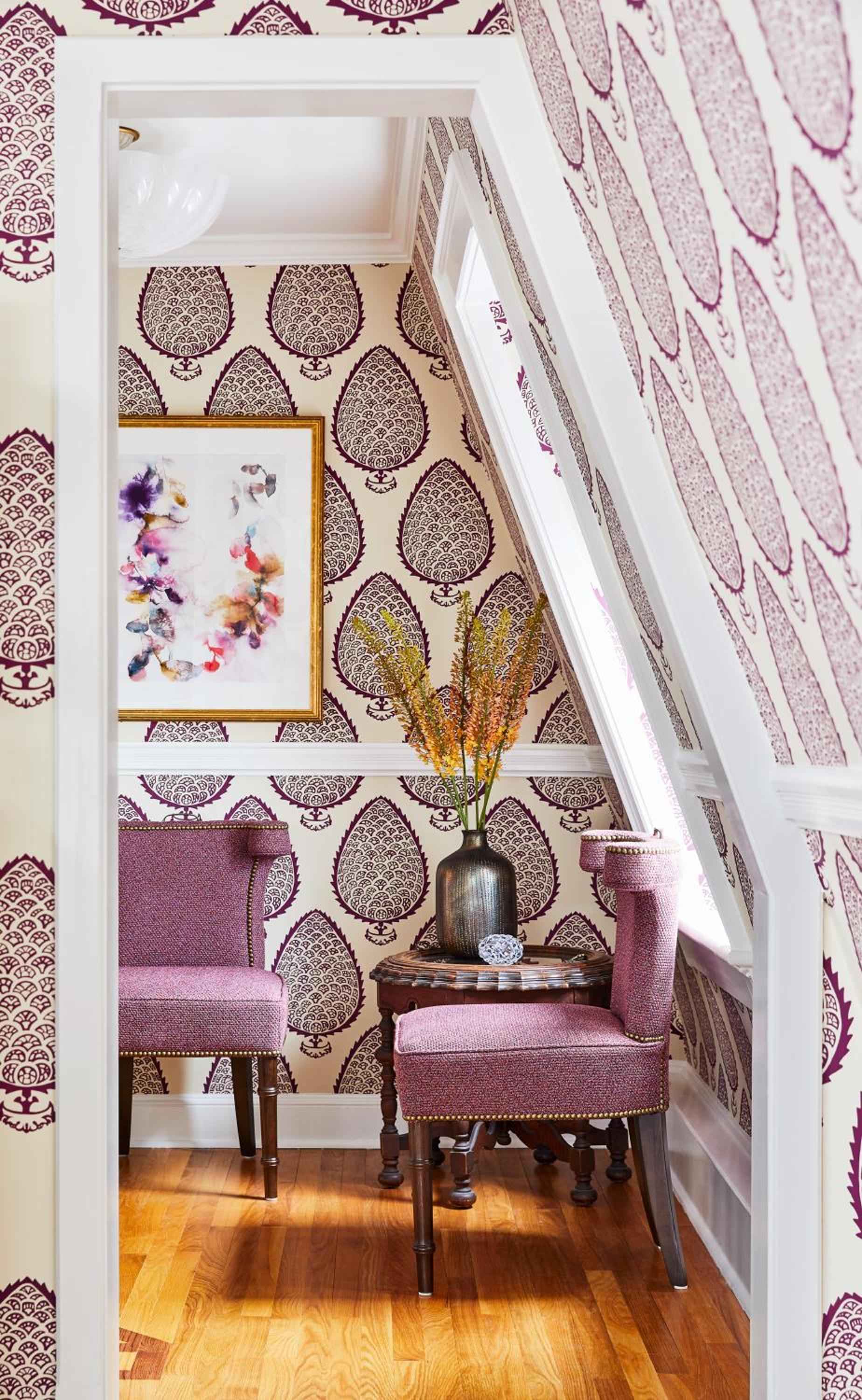 Bold burgundy paisley wallpaper transforms a cozy reading nook, where purple velvet chairs frame golden dried wheat and warm hardwood floors create intimate charm.