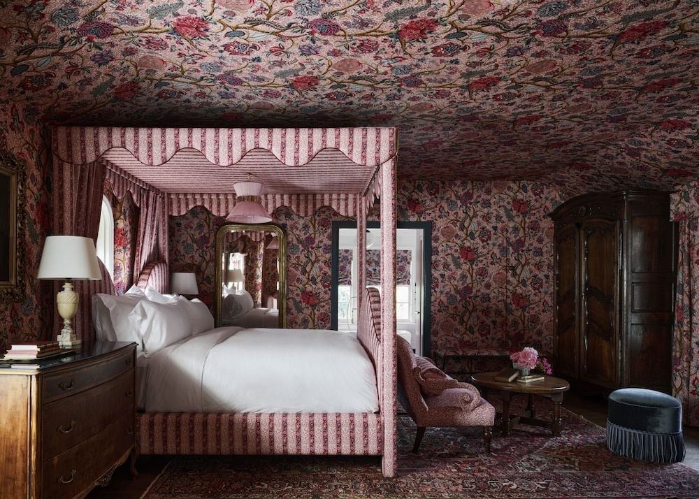 Burgundy florals bloom across walls and ceiling in this intimate four-poster suite, where striped canopy bed linens create a cocoon of English countryside elegance.