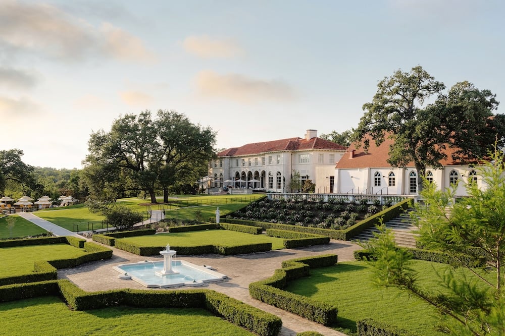 Manicured parterre gardens unfold like a green tapestry beneath the mansion's coral-tiled roofs, where geometric hedgerows frame a central fountain in perfect symmetry.