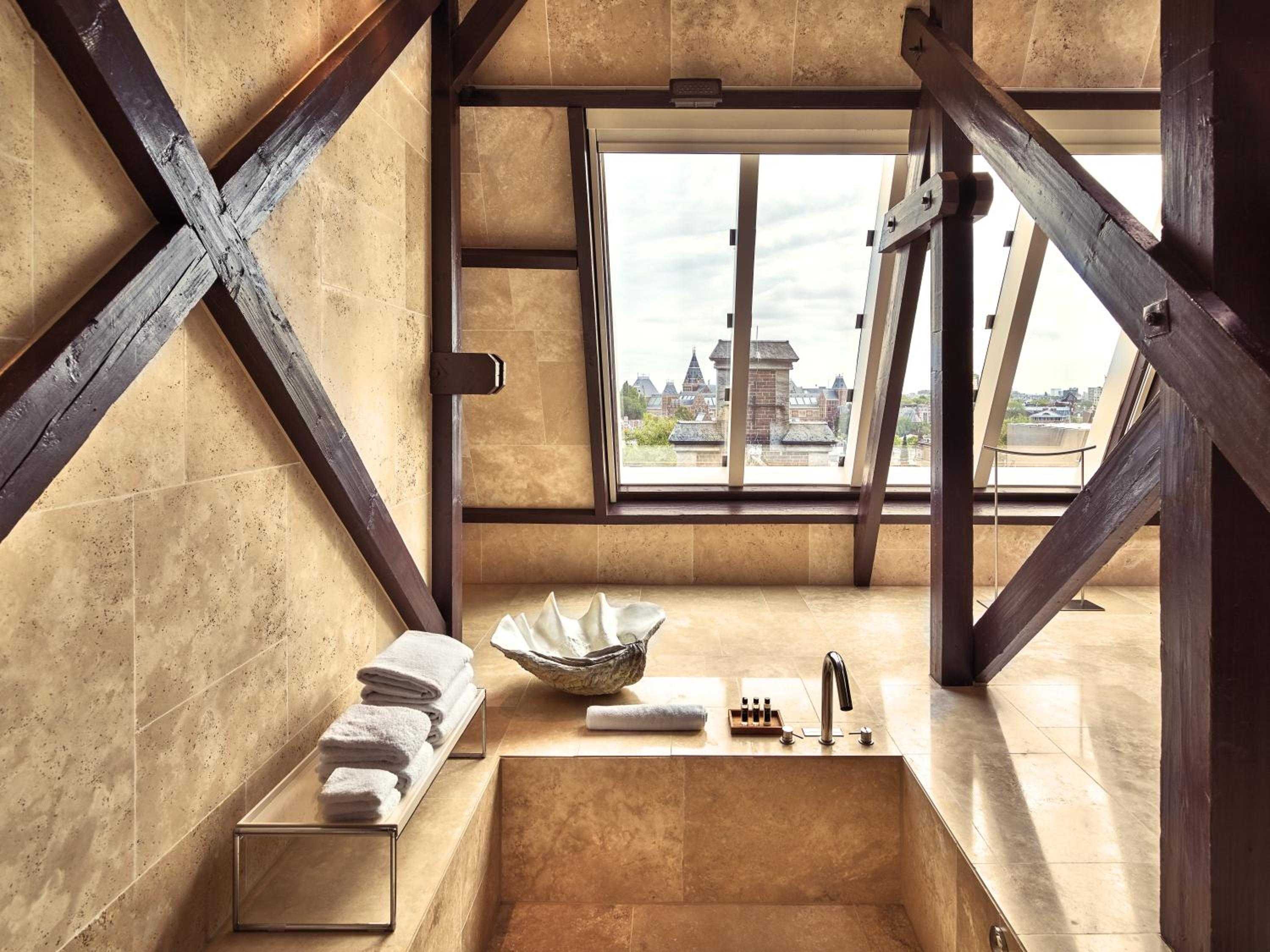 Exposed timber beams frame a limestone sanctuary where modern luxury meets historic architecture, creating an intimate bathing retreat high above Amsterdam's rooftops.