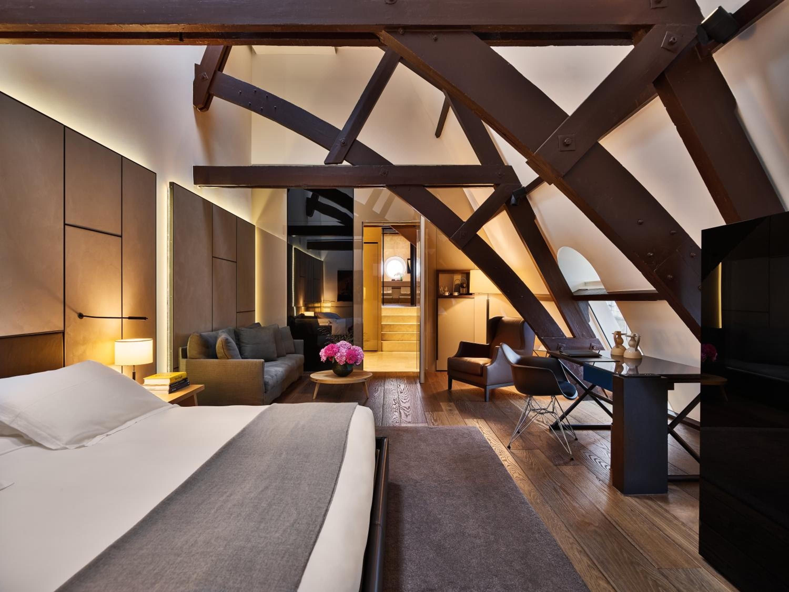 Exposed timber beams frame this sophisticated attic suite where contemporary luxury meets historic architecture, creating an intimate retreat beneath Amsterdam's rooflines.