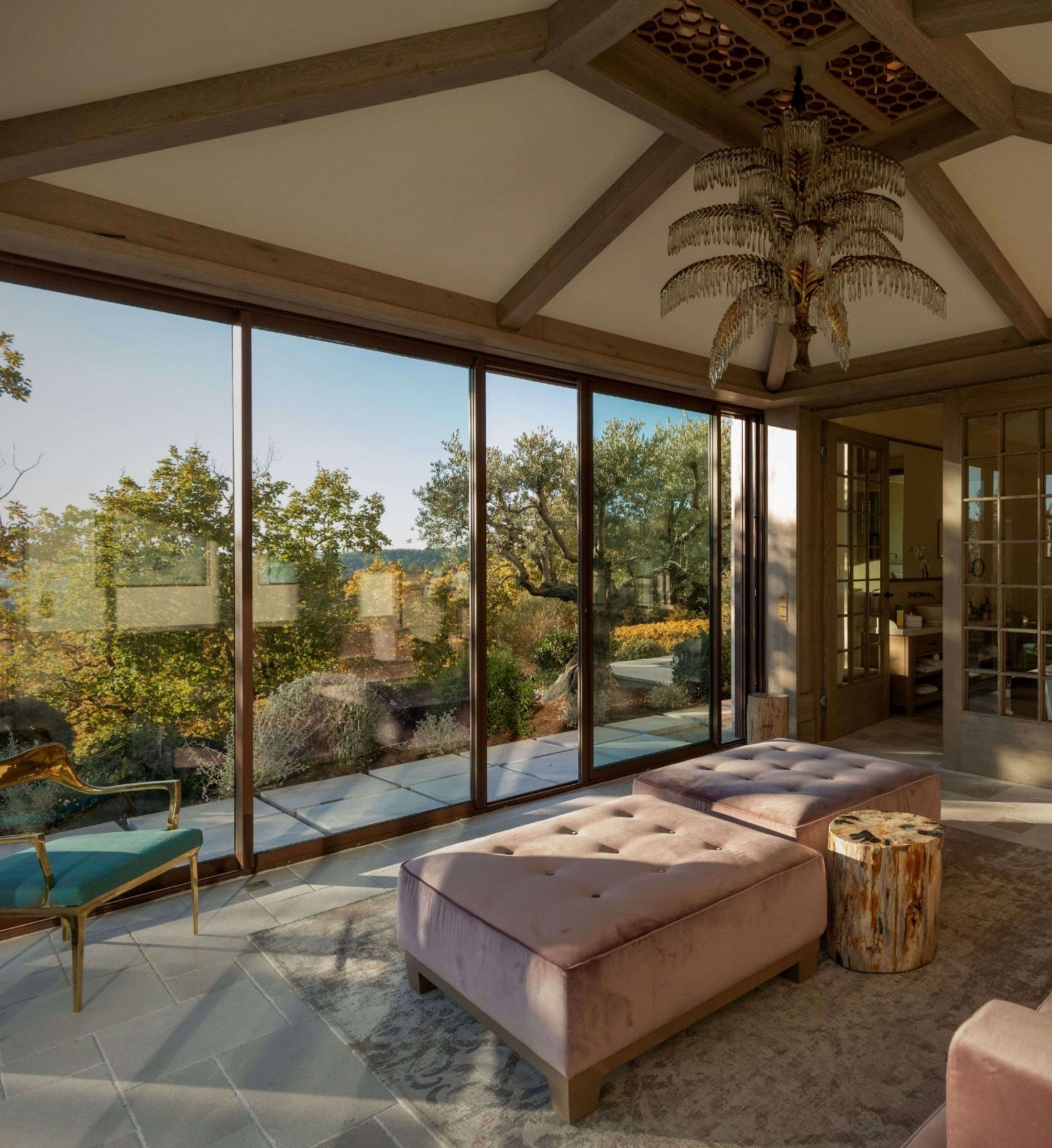 Sunlight filters through floor-to-ceiling windows onto plush velvet ottomans, while an ornate chandelier crowns this elegant living space overlooking Provence's rolling vineyard landscape.